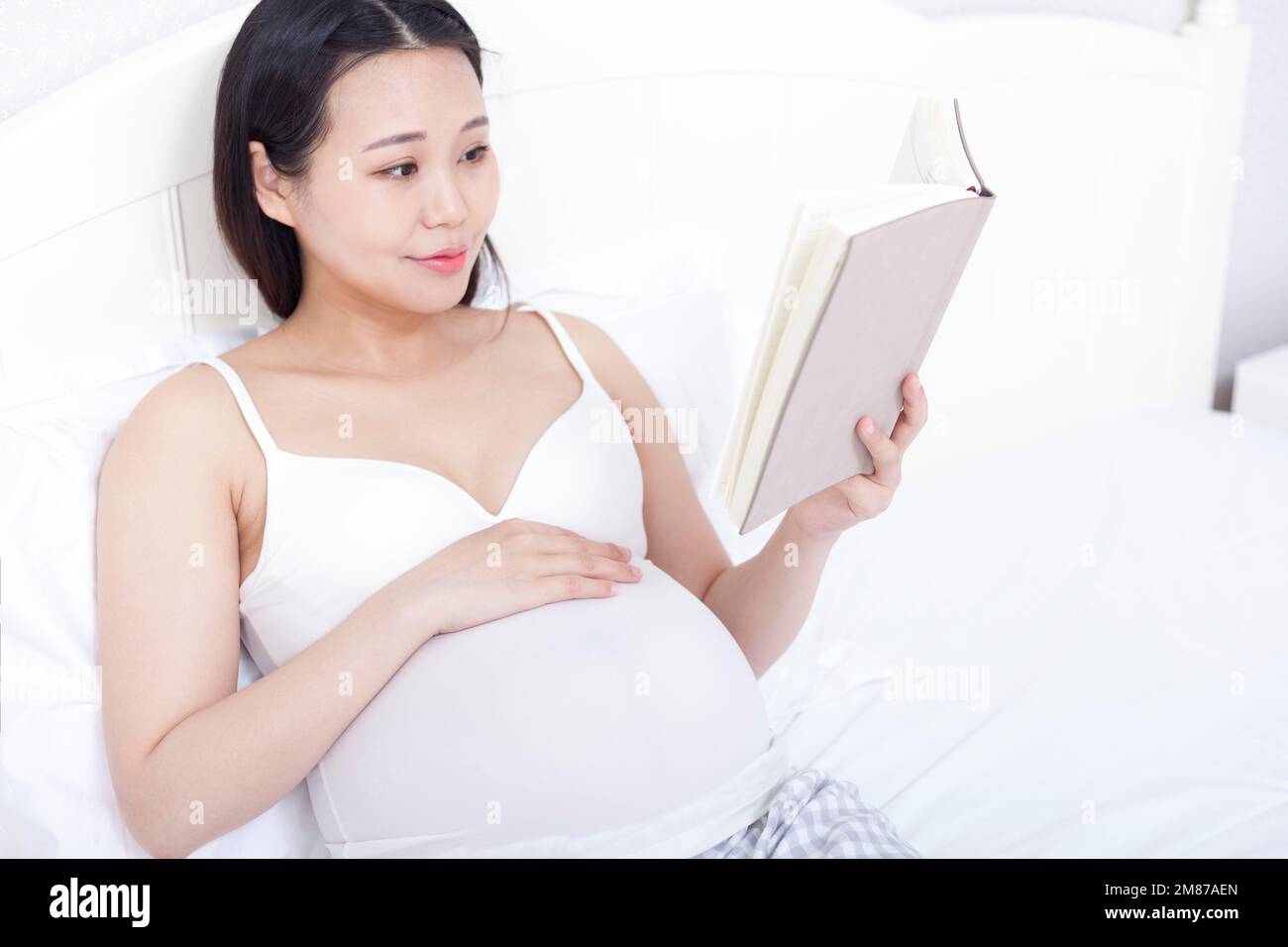 Les femmes enceintes se sont assises au lit pour lire un livre Banque D'Images