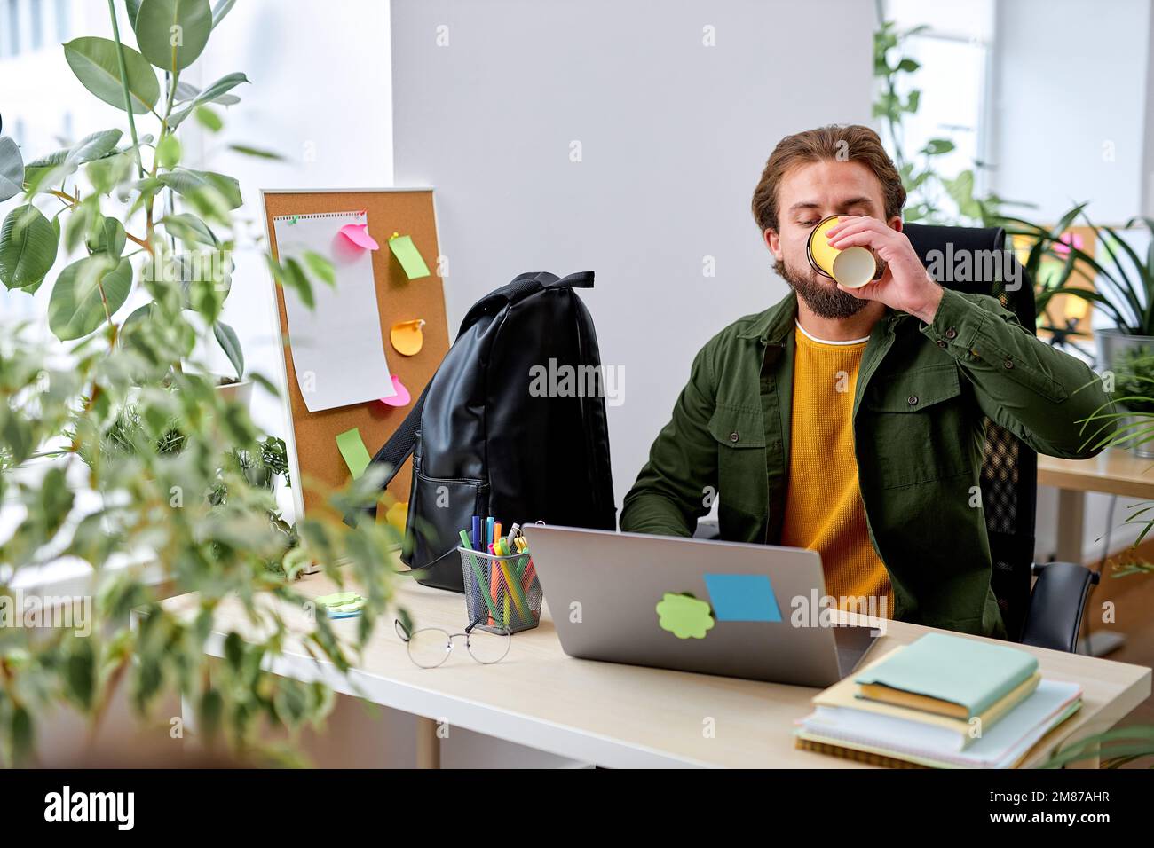 Un homme barbu travaille sur un ordinateur portable dans un bureau buvant du café, seul, le succès et le concept d'entreprise. Beau homme sympa dans une tenue décontractée est concentré sur le travail Banque D'Images