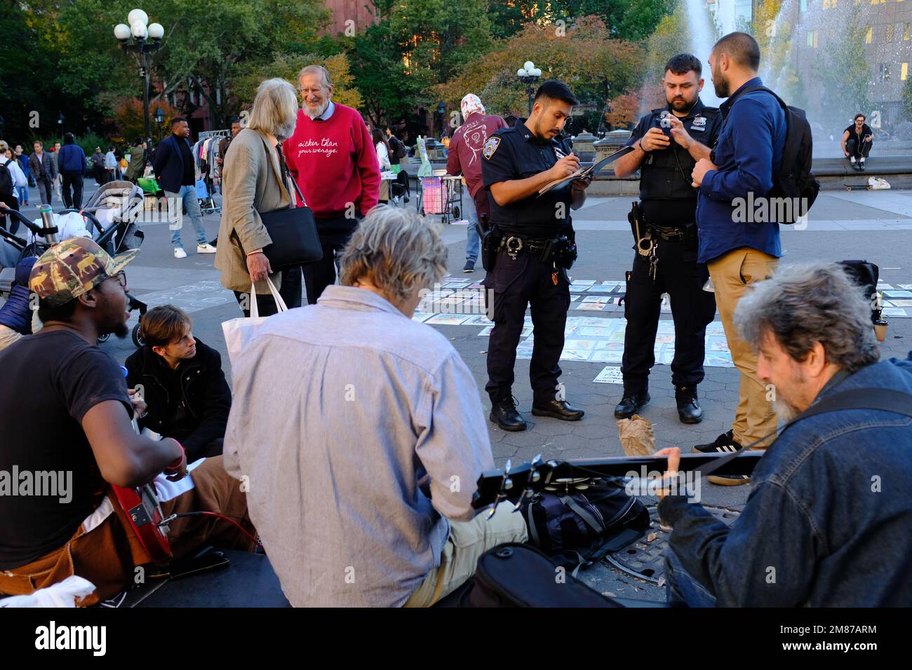 Deux policiers de la NYPD délivrant un billet d'amende à un homme qui boit de l'alcool à Washington Square Park avec un groupe de musiciens jouant de la musique à Foreground.Manhattan.New York City.USA Banque D'Images