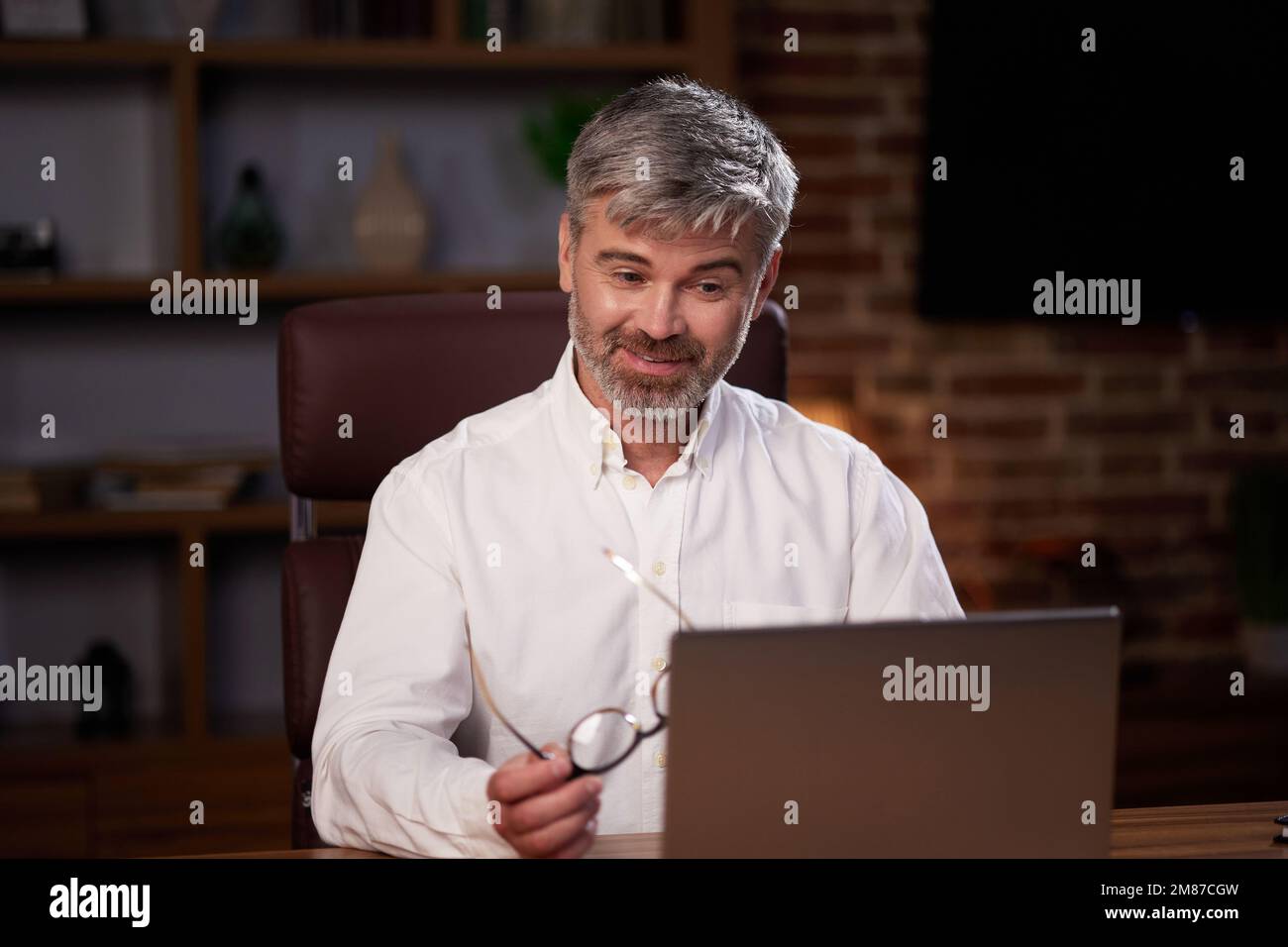 Homme âgé aux cheveux gris travaillant au bureau à domicile avec un ordinateur portable. Portrait d'affaires d'un beau responsable assis sur le lieu de travail. Étudier des cours en ligne Banque D'Images