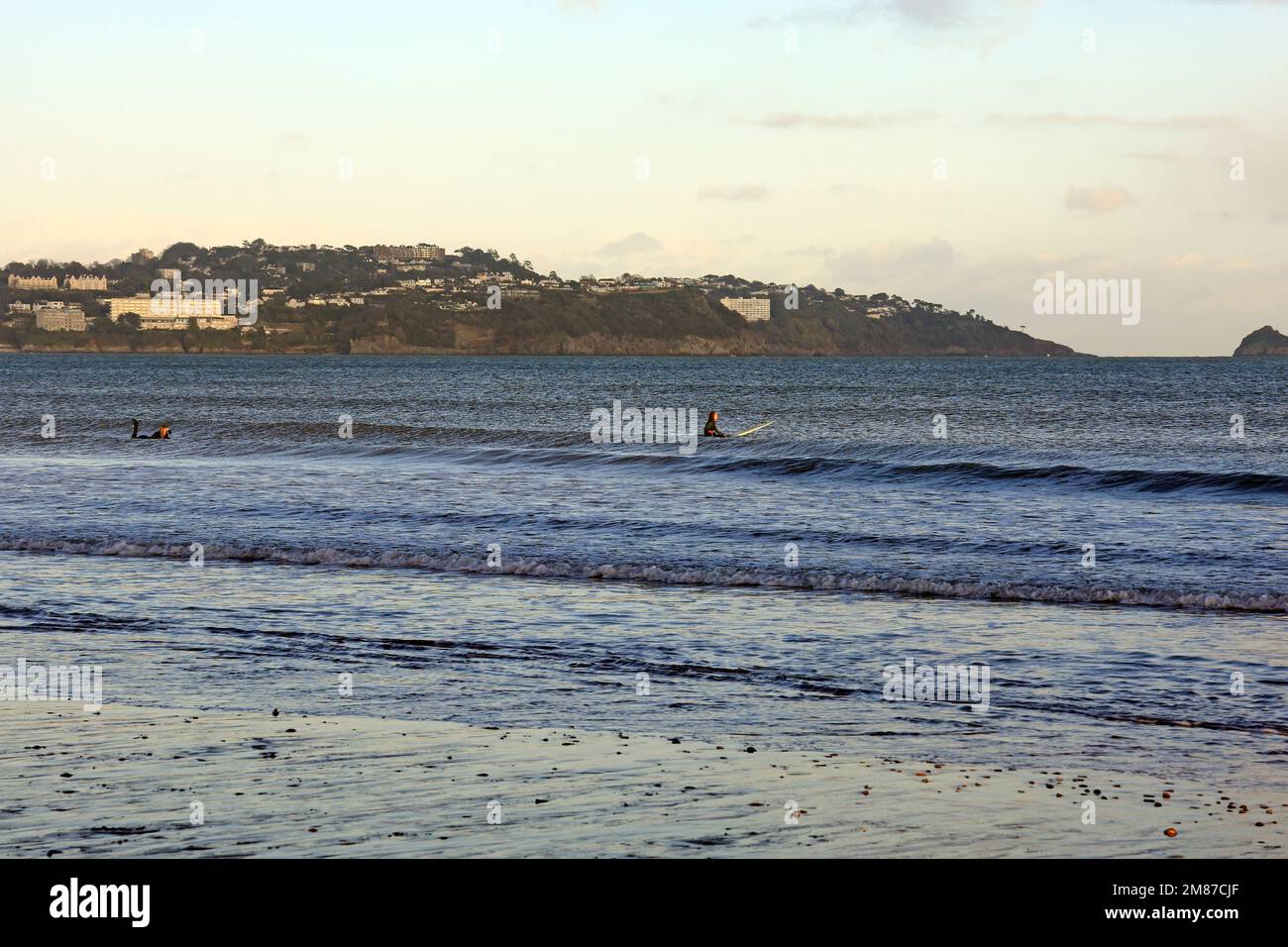 Deux jeunes femmes en combinaisons mouillées surfant sur de petites vagues près de la rive à Paignton, prises le 2023 janvier. Hiver Banque D'Images