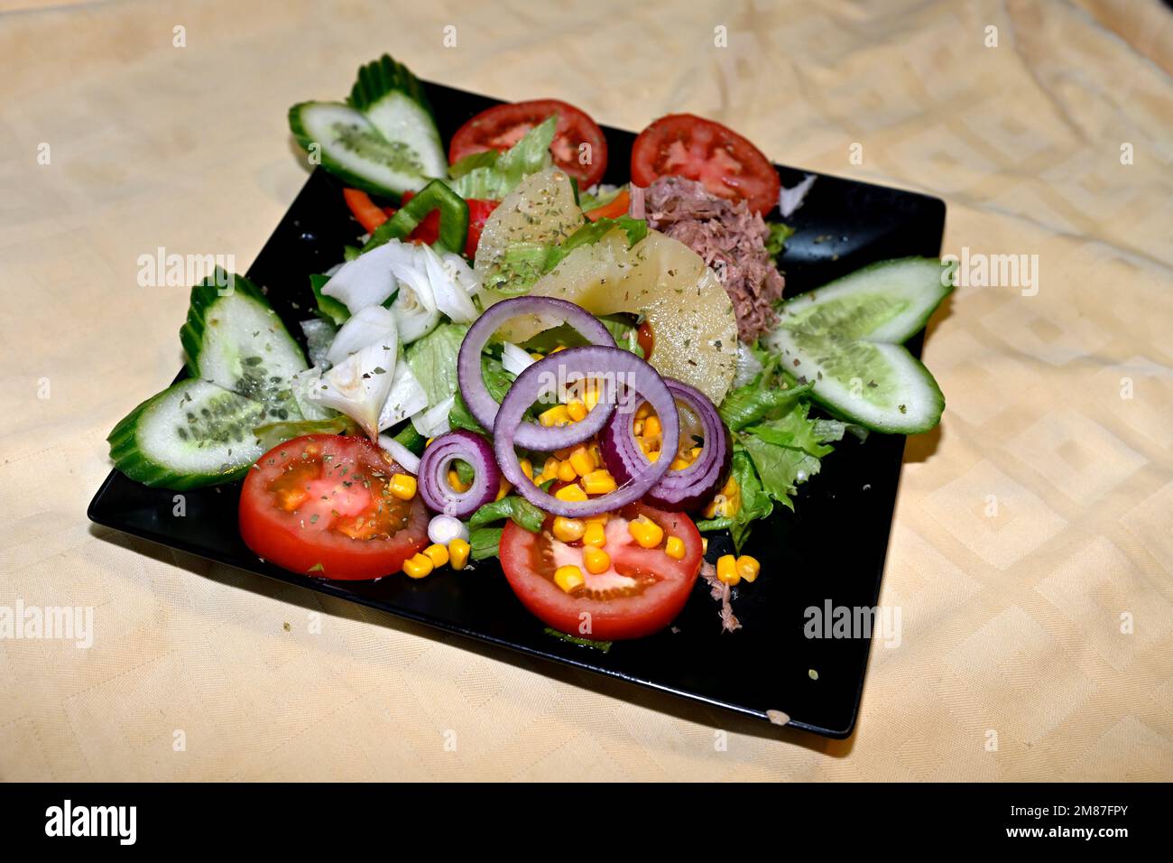 Assiette de salade mixte, tomate, concombre, oignon, poivron vert, maïs, ananas avec origan sur plaque carrée noire Banque D'Images