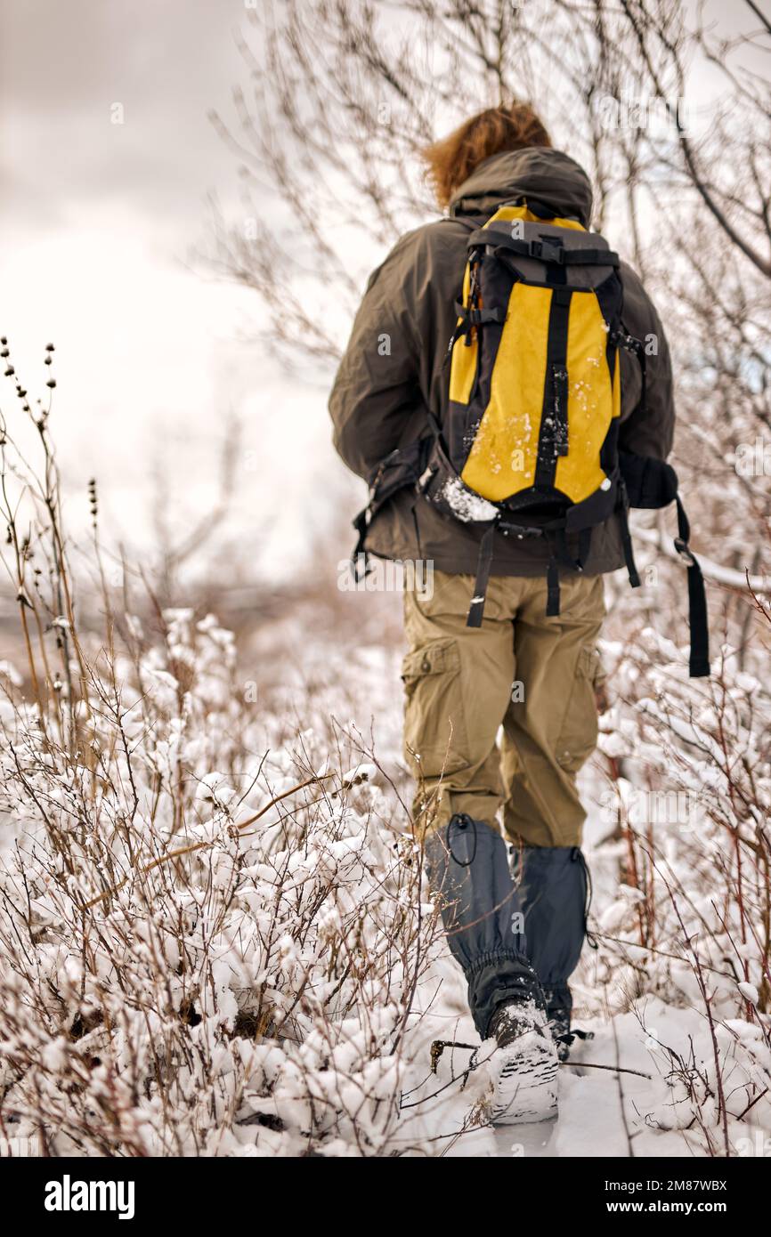 vue arrière sur un homme chaud veste manteau et sac à dos marche le long  d'un chemin couvert de neige vers les montagnes. Beau paysage avec neige et  forêt sur nuageux Photo