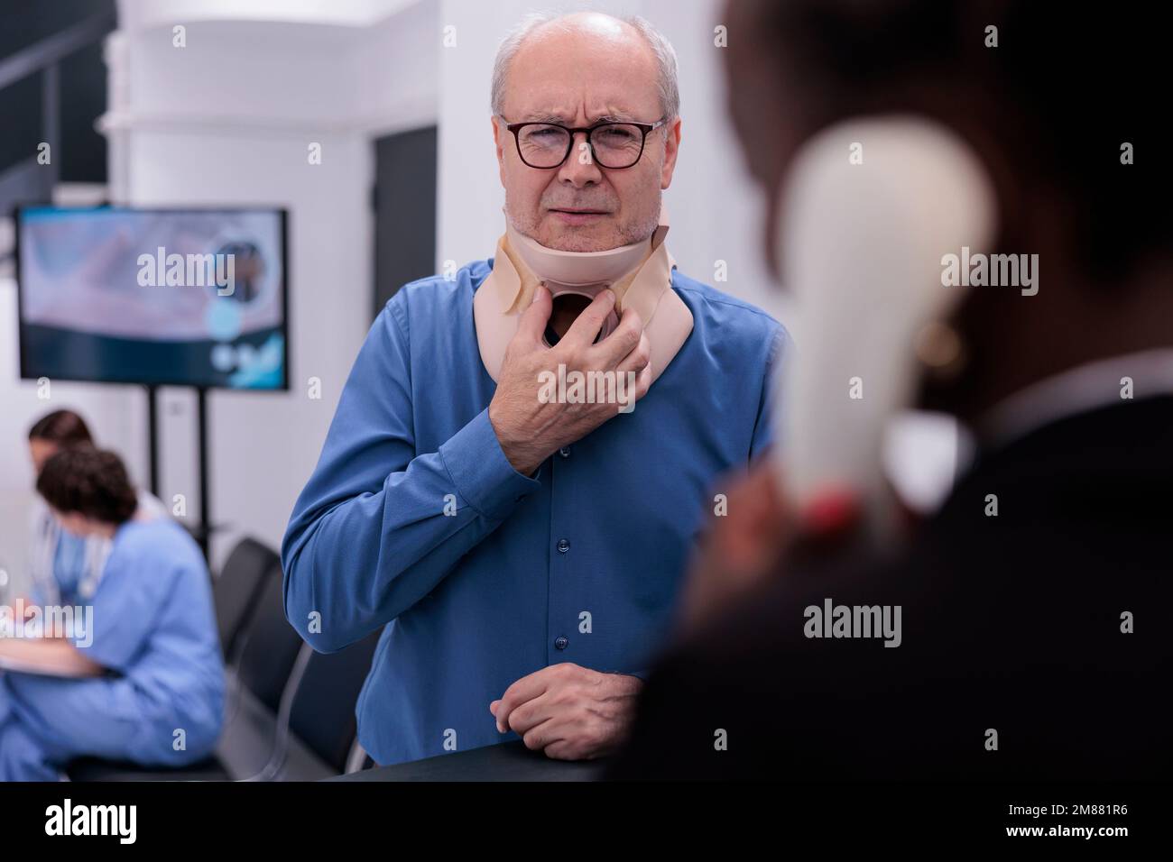 Patient âgé blessé avec col cervical discutant avec un employé de l'accueil lors d'un rendez-vous de visite de contrôle dans la salle d'attente de l'hôpital. Service et concept de soutien des soins de santé Banque D'Images