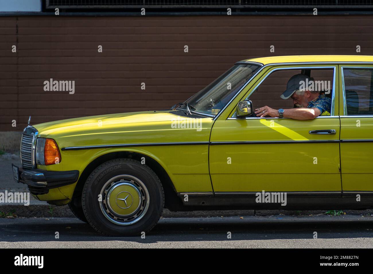 Homme allemand senior assis dans une Mercedes jaune vif tout en tenant une cigarette dans sa main, coude hors de la fenêtre. Berlin, Allemagne Banque D'Images