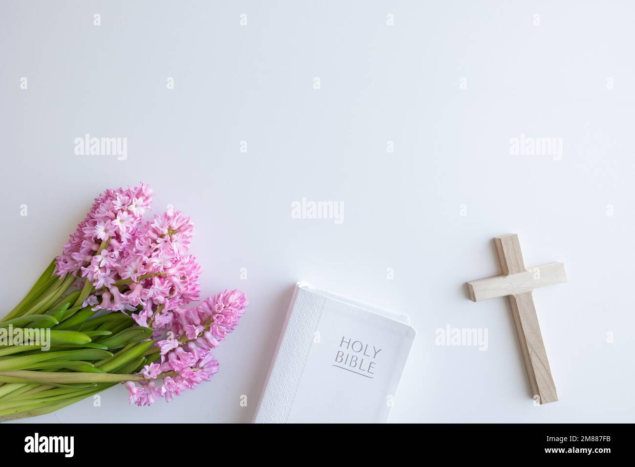 Bordure de la Bible chrétienne blanche, petite croix de bois et bouquet de fleurs de jacinthe rose sur fond blanc avec espace de copie Banque D'Images
