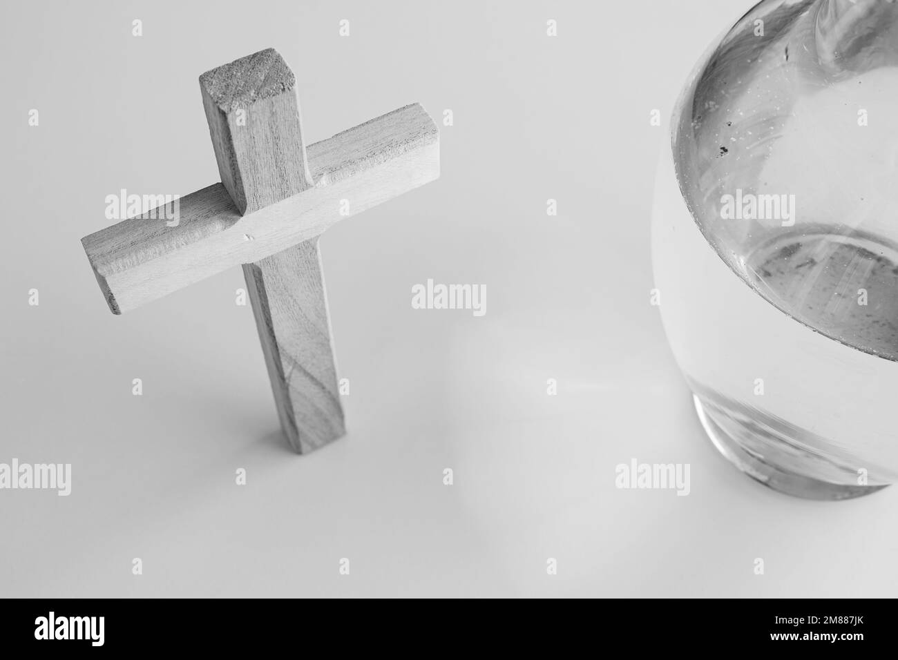 Simple croix chrétienne en bois et un pot d'eau en verre transparent sur fond blanc avec espace de copie Banque D'Images