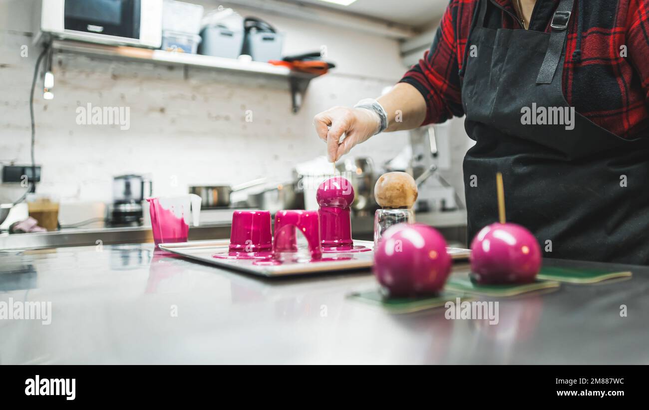 vue latérale d'un boulanger décorant des boules de chocolat avec de la crème rose dans la boulangerie, concept de dessert. Photo de haute qualité Banque D'Images