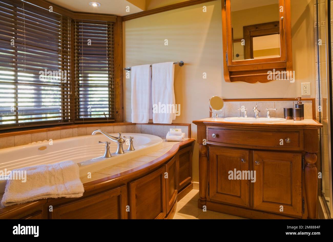 Jacuzzi ovale et meuble-lavabo en bois dans la chambre d'hôtes au sous-sol,  salle de bains attenante à l'intérieur d'une luxueuse maison en rondins de  style scandinave, Québec, Canada. Cette image est p