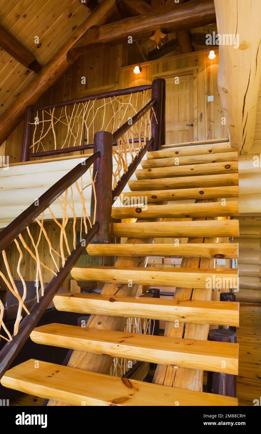 Escaliers en bois de pin blanc avec rambardes de cèdre menant à l'étage supérieur à l'intérieur de la maison en rondins de style scandinave. Banque D'Images