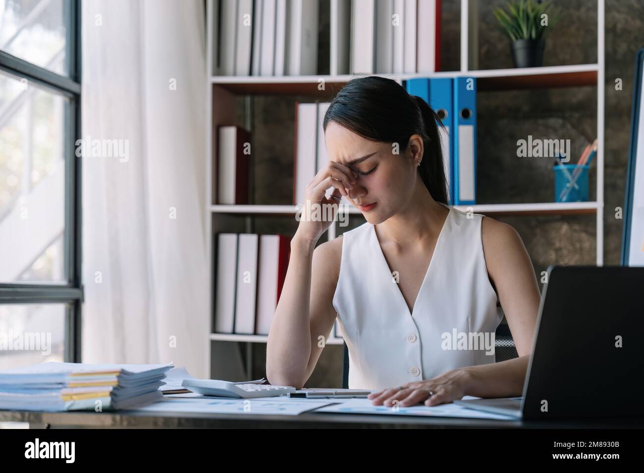 Femme asiatique stressée en travaillant sur ordinateur portable, femme d'affaires asiatique fatiguée avec mal de tête au bureau, se sentant malade au travail Banque D'Images