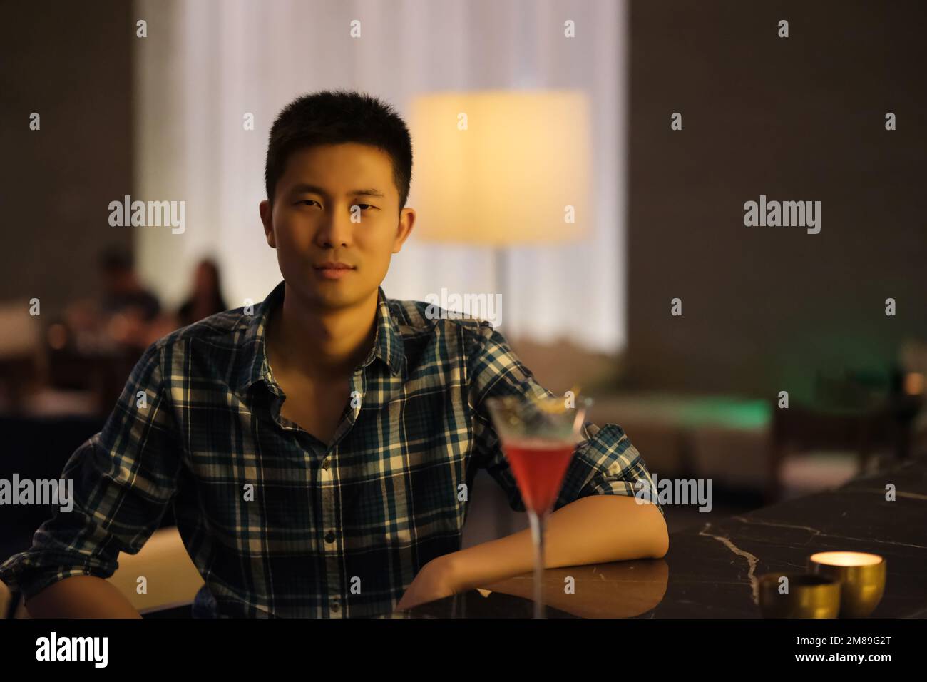 Portrait d'un beau jeune asiatique assis au comptoir du bar de nuit, avec un verre de cocktail, regardant l'appareil photo Banque D'Images