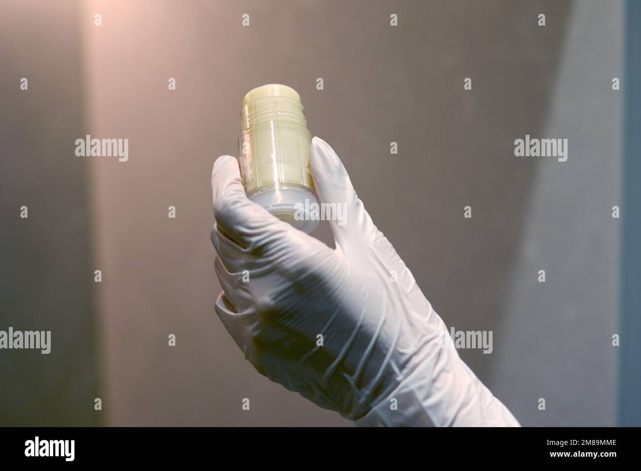 Main gantée tenant une bouteille de baume cosmétique en laboratoire Banque D'Images
