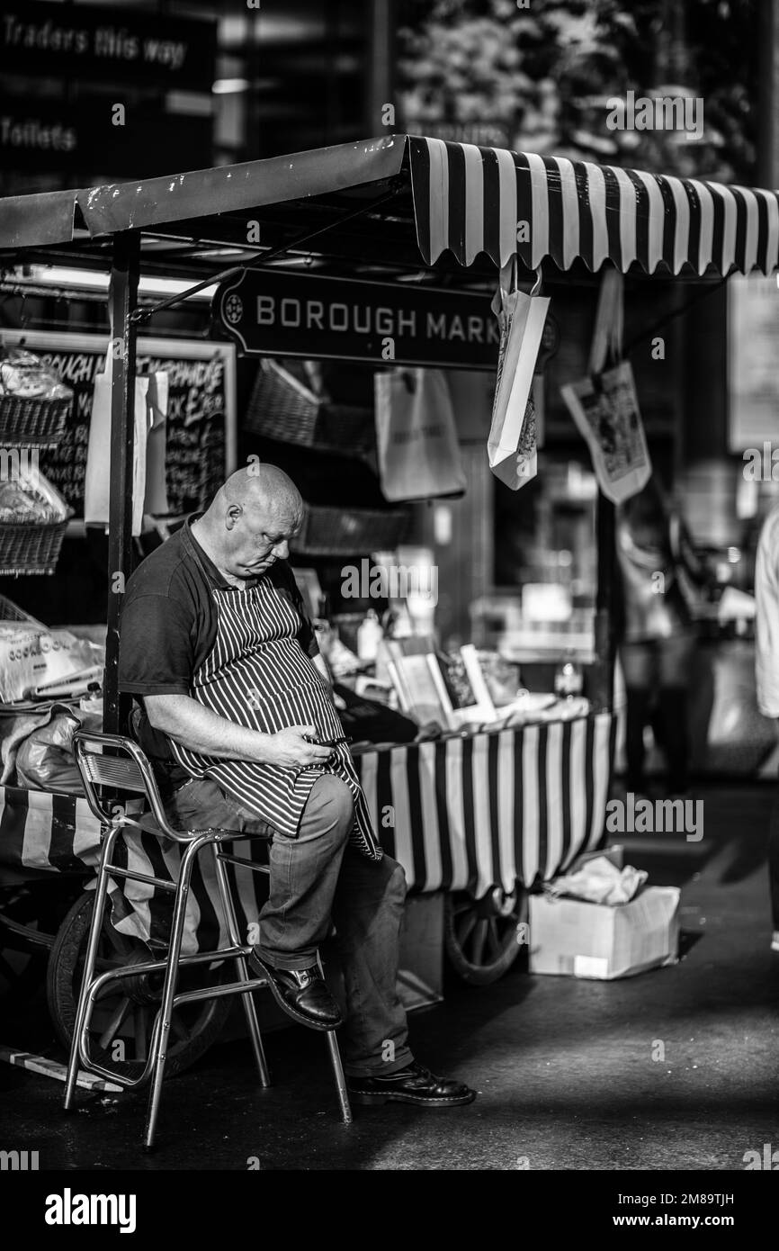 Un vertical d'homme caucasien dans un tablier assis à Borough Market à Londres, Angleterre tourné en niveaux de gris Banque D'Images