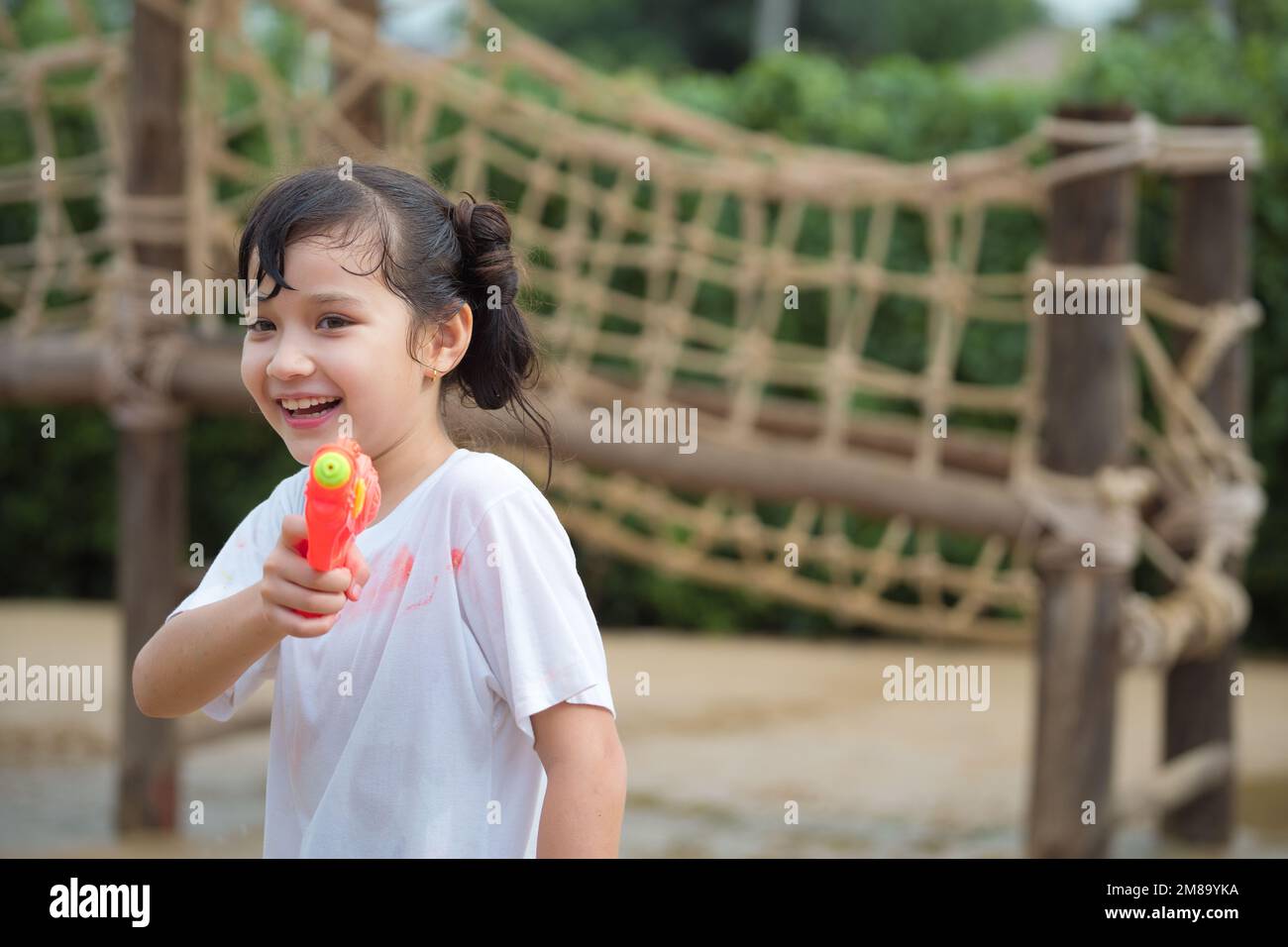 Happy Child girl s'amuse à jouer au tir au pistolet à eau sur une aire de jeux en plein air le jour d'été chaud à l'extérieur. Banque D'Images