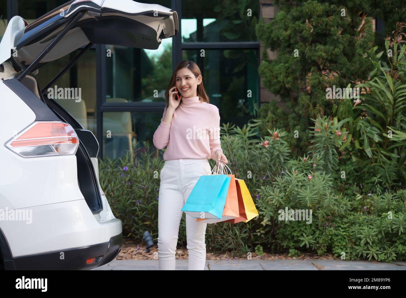 Une jeune femme met des sacs d'achats dans la voiture et parle au téléphone. Banque D'Images