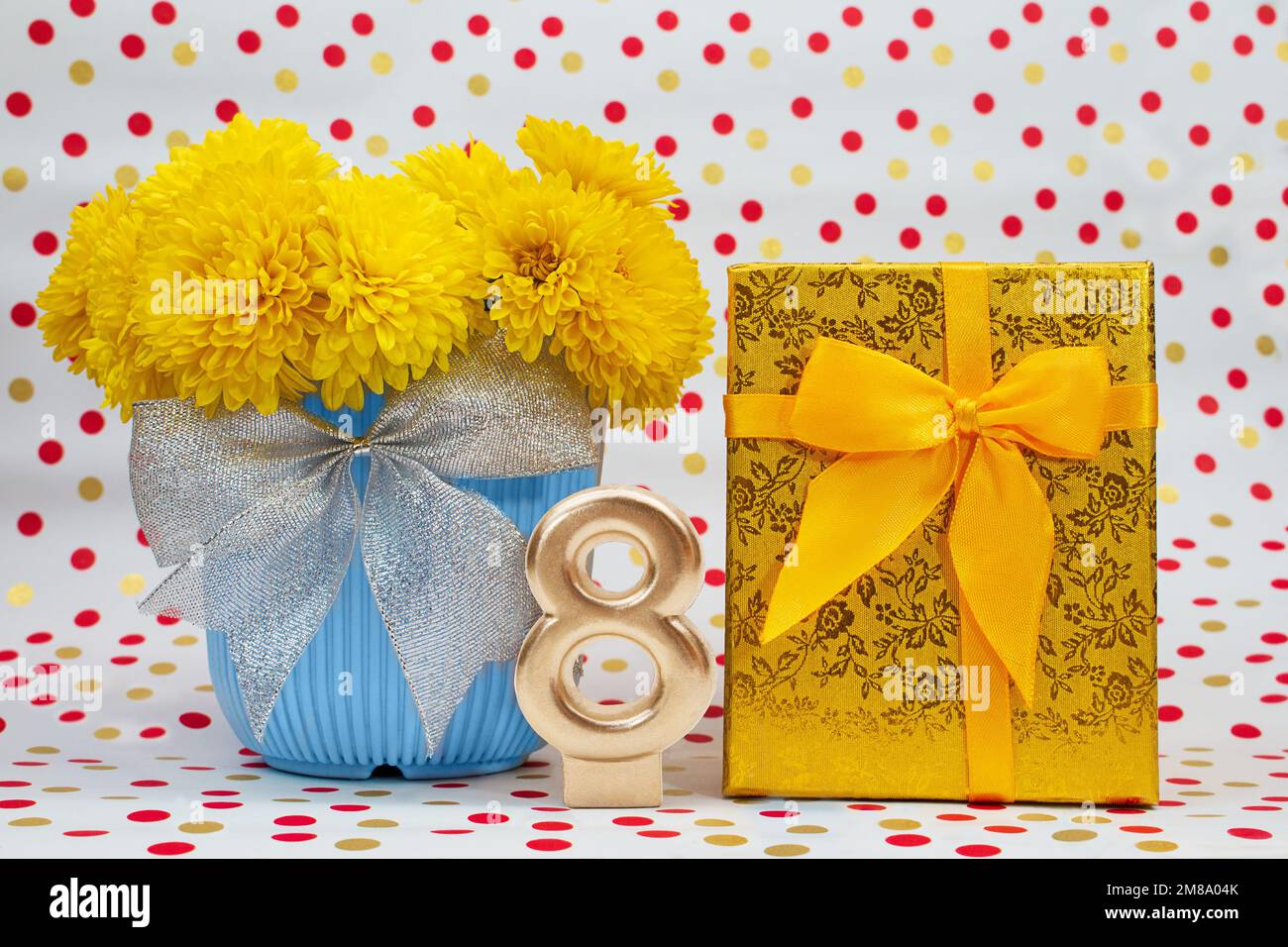 Bouquet de chrysanthèmes jaunes en pot bleu avec noeud et boîte cadeau dorée, numéro 8, derrière fond blanc avec pois. International Women's Da Banque D'Images