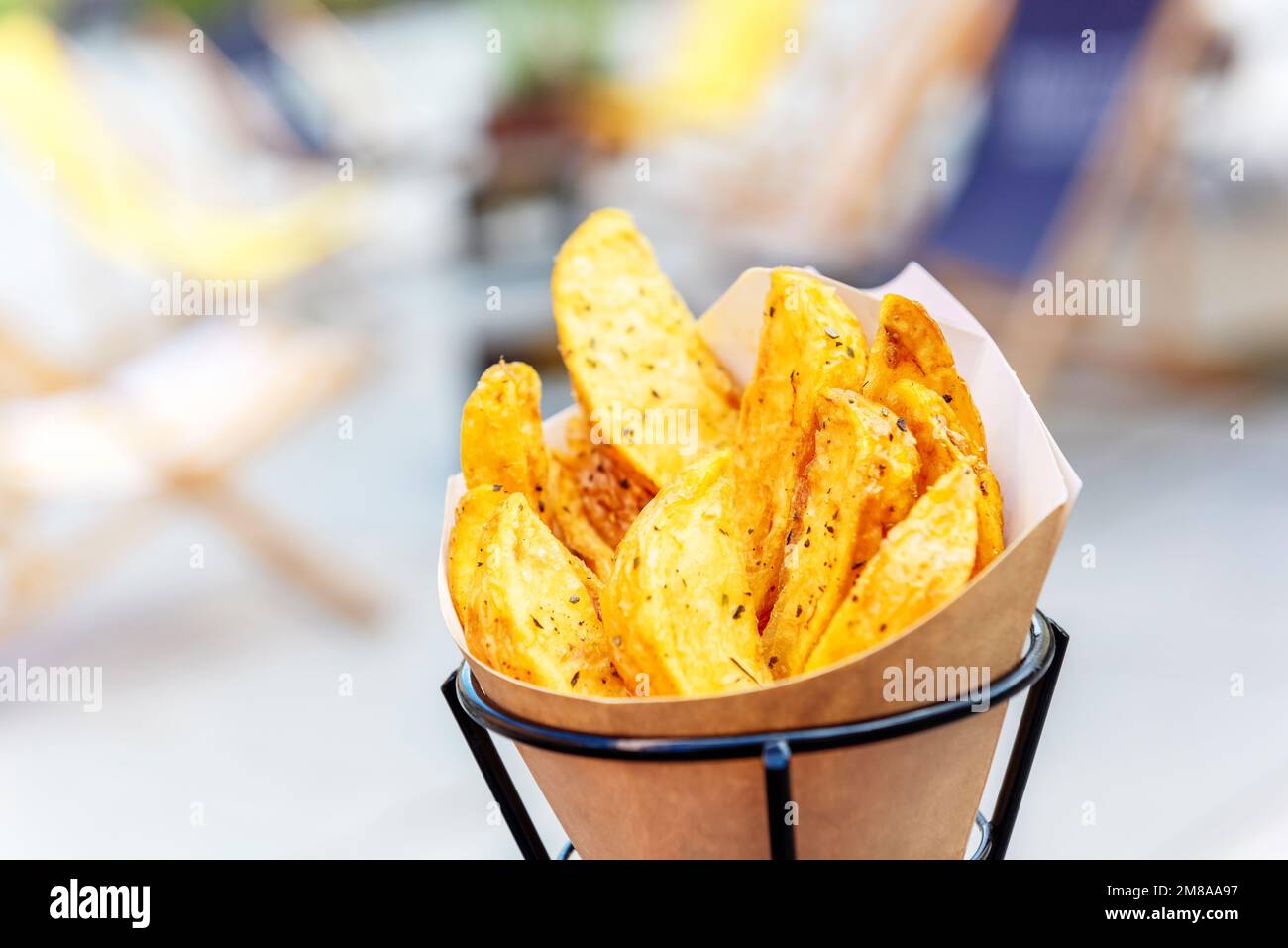 Quartiers de pommes de terre cuits au four avec sel de mer et herbes. frites dans un sac en papier recyclable sur un fond de rue flou, fast food populaire Banque D'Images