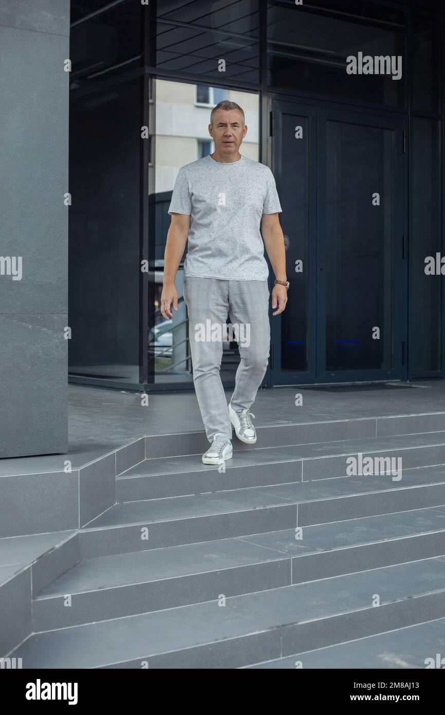 Homme aux cheveux gris plein d'assurance, vêché d'une tenue grise près du mur, près de l'entrée à l'extérieur. Recrutement, trouver un nouvel emploi, service RH Banque D'Images