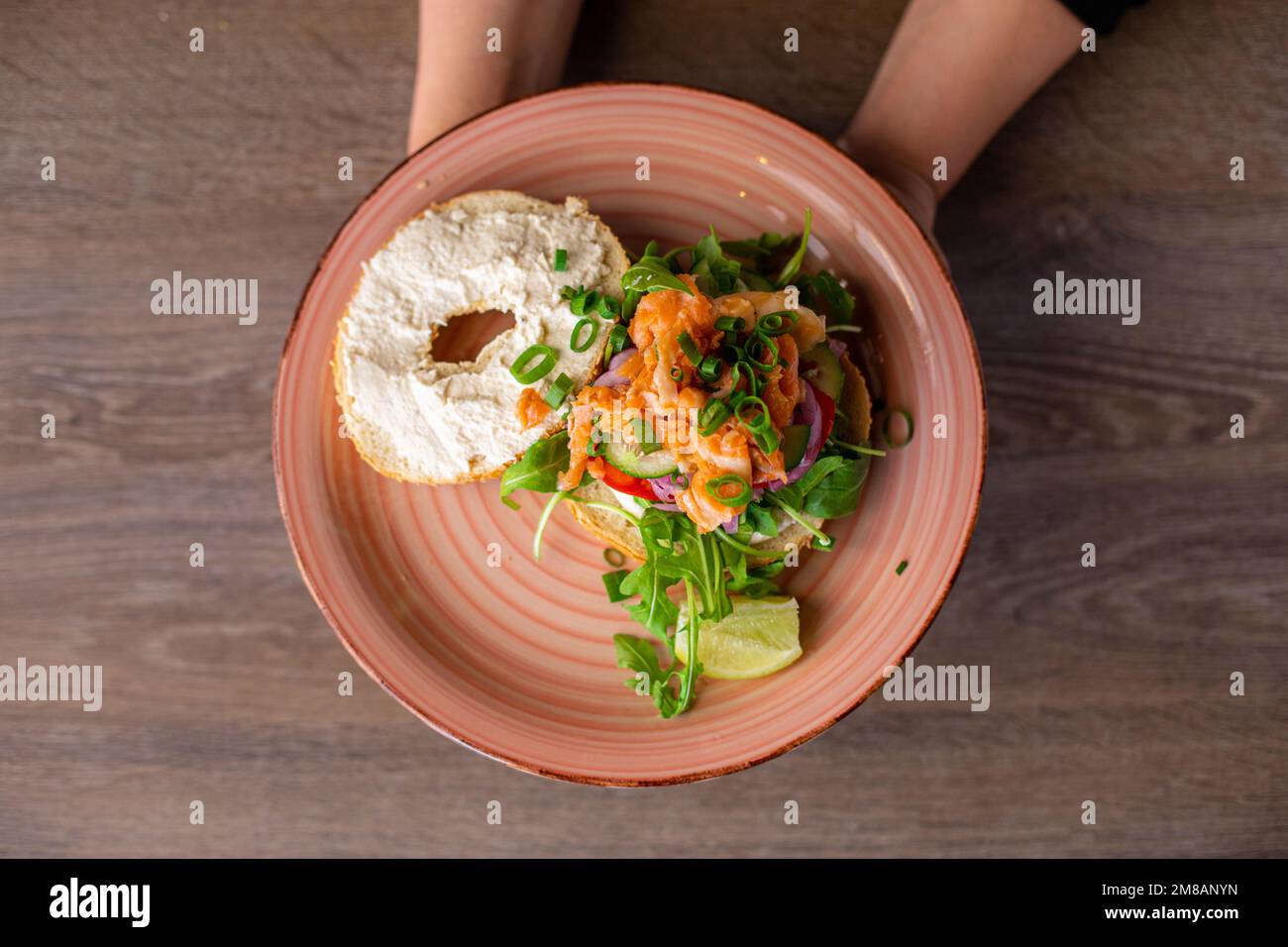 Photo rognée d'une femme tenant une assiette rose avec un hamburger plein de saveur avec trou dans un petit pain, saumon coupé, arugula, verdure. Banque D'Images Photo rognée d'une femme tenant une assiette rose avec un hamburger plein de saveur avec trou dans un petit pain, saumon coupé, arugula, verdure. Banque D'Images