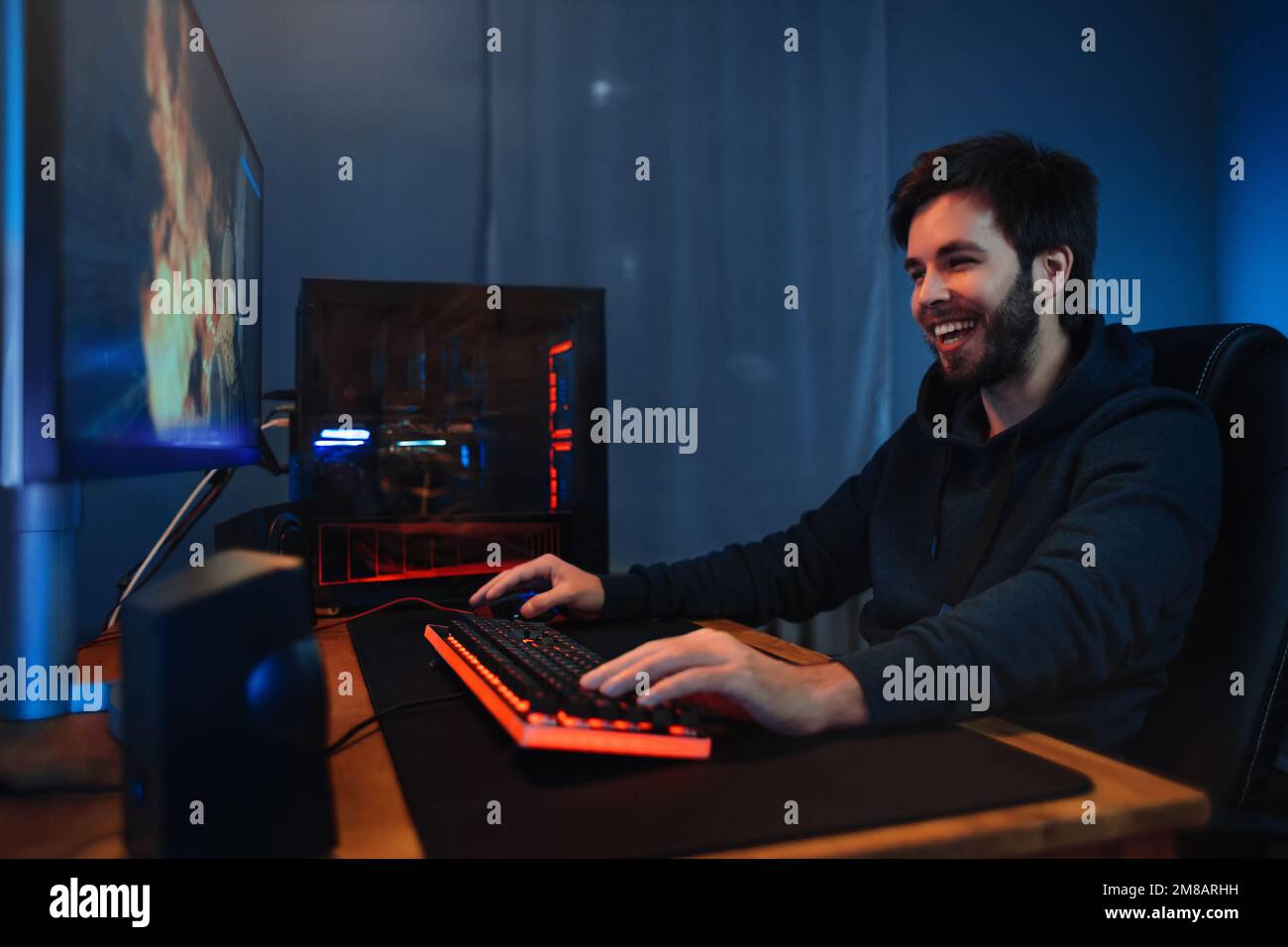 Un jeune gamer de race blanche apprécie de jouer dans un jeu de tir en ligne. Il passe sa soirée à la maison à jouer à des jeux vidéo sur ordinateur avec des amis. Cybersport, addiction informatique. Vue latérale, néon Banque D'Images