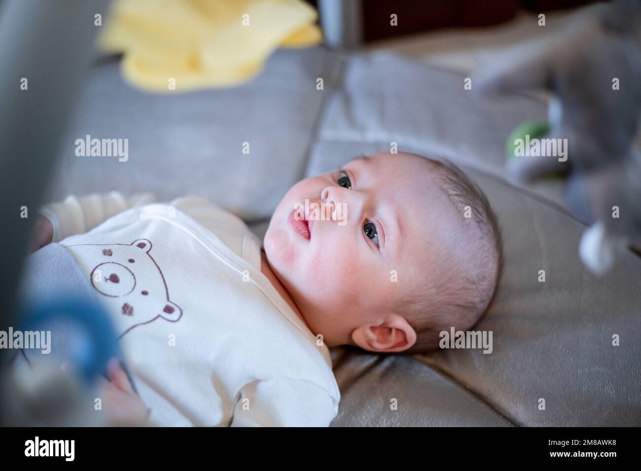 Un petit garçon de 3 à 6 mois allongé sur le dos à l'intérieur d'une salle de gym pour bébé et regardant des jouets suspendus avec une expression faciale sérieuse Banque D'Images