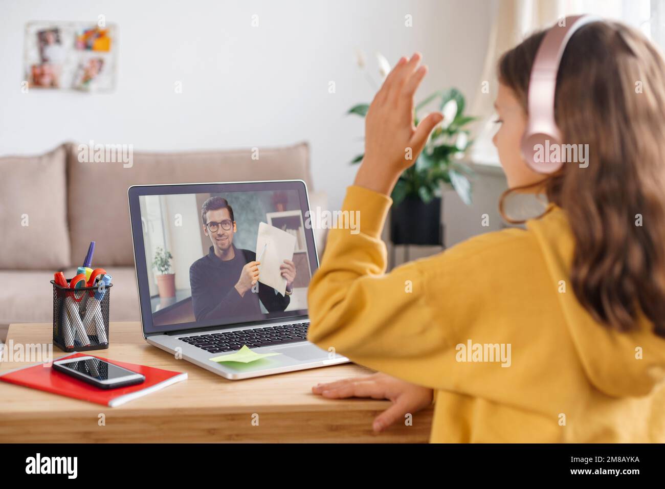 La jeune fille étudie à distance, en utilisant la webcam pour ordinateur portable et le casque, lève sa main pour répondre à la question de l'enseignant. Enseignement à domicile et enseignement à distance. Tuteur en ligne ayant une leçon à distance Banque D'Images