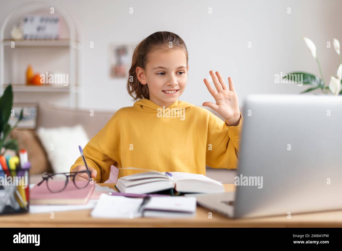 Souriant petite fille caucasienne ayant vidéo appel classe distante avec professeur d'école, en utilisant un ordinateur portable, la main, saluant tuteur personnel, étudiant en ligne sur ordinateur. Homeschooling et enseignement à distance Banque D'Images