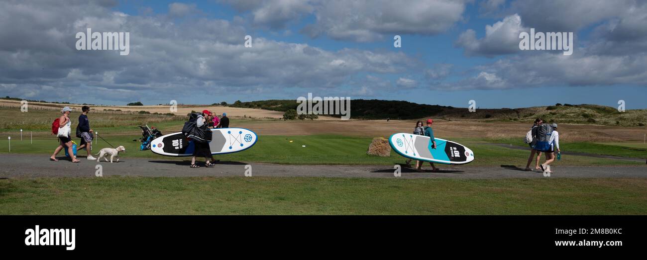 Les surfeurs et les randonneurs se promènaient jusqu'à la plage d'Embleton, Northumberland, Royaume-Uni. Il y a une promenade jusqu'à Craster qui passe devant le château de Dunstanburgh en ruines. Banque D'Images