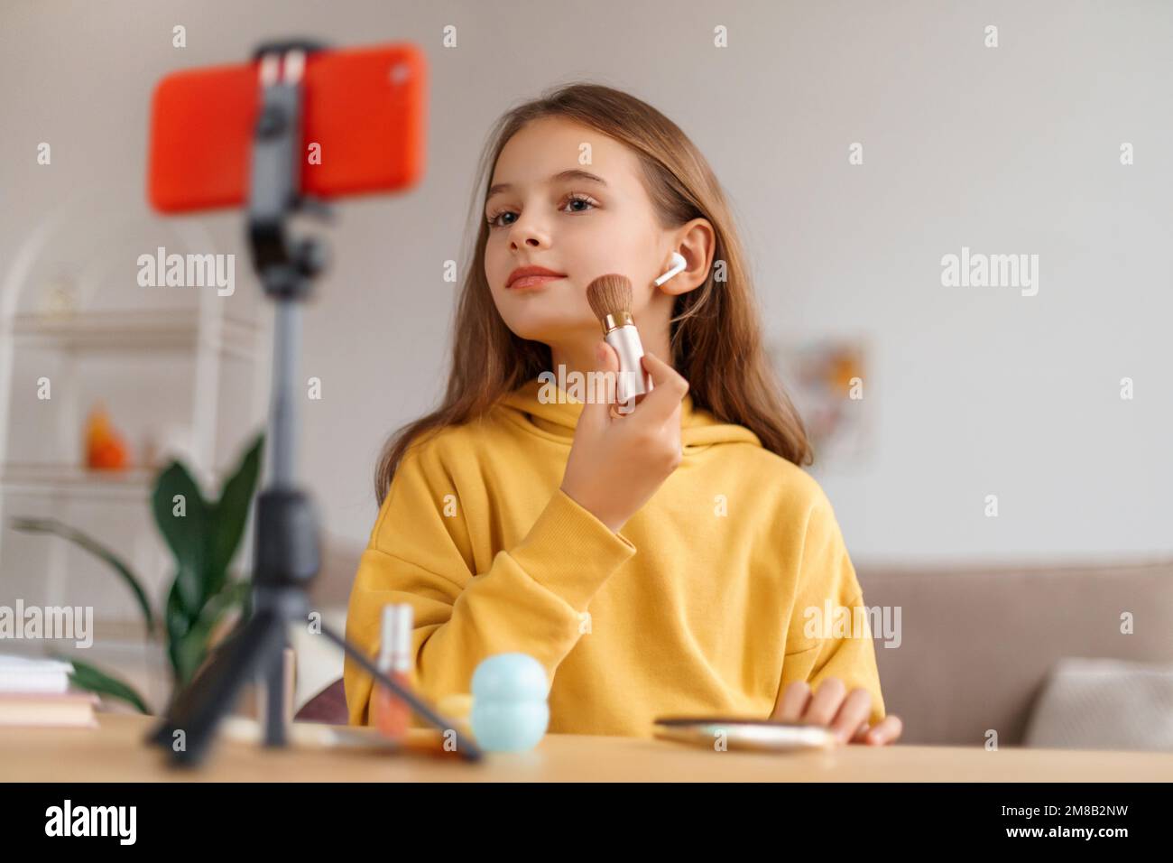 Sourire fille beauté blogueur enregistrement vlog à la maison, regardant le smartphone sur trépied au bureau, tournage en ligne tutoriel, montrant comment utiliser cosmétique, faire le maquillage sur la webcam. Concept de réseaux sociaux pour enfants Banque D'Images