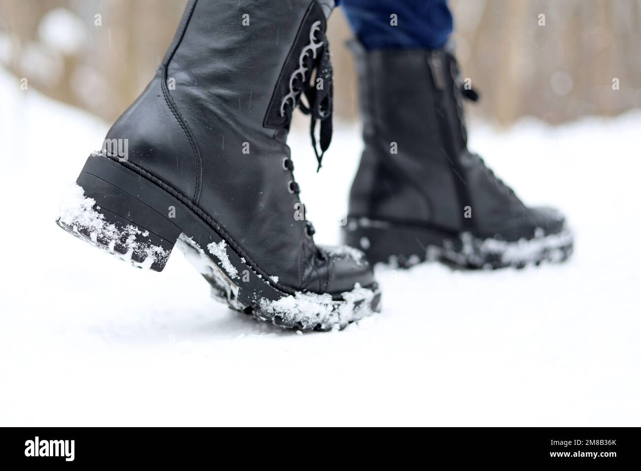 Jambes de femme en cuir noir bottes à lacets sur la neige.Femme marchant sur la rue d'hiver, chaussures chaudes pour temps froid Banque D'Images