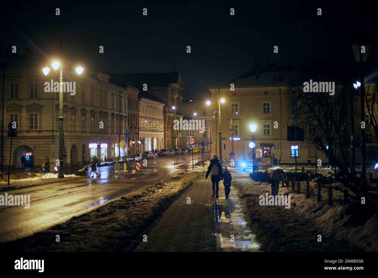 Nuit d'hiver rue de Cracovie avec lumières et lanternes. Une femme avec des enfants marche. Banque D'Images