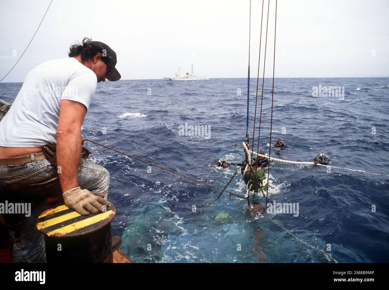 Des plongeurs du 1730th Pararescue Squadron surveillent les progrès d'un hélicoptère géant HH-3E Jolly Green de la Force aérienne qui est soulevé par une grue à bord du navire de sauvetage japonais SHIN TATSU MARU. L'hélicoptère, qui s'est écrasé dans l'océan à 5,6 milles au large de la côte d'Okinawa, au Japon, est récupéré par une équipe de sauvetage conjointe États-Unis/Japon. Un grand navire de patrouille de classe Shiretoko de l'Agence japonaise de sécurité maritime à proximité garde la zone dégagée au fur et à mesure que l'opération progresse. Pays : Océan Pacifique (POC) Banque D'Images