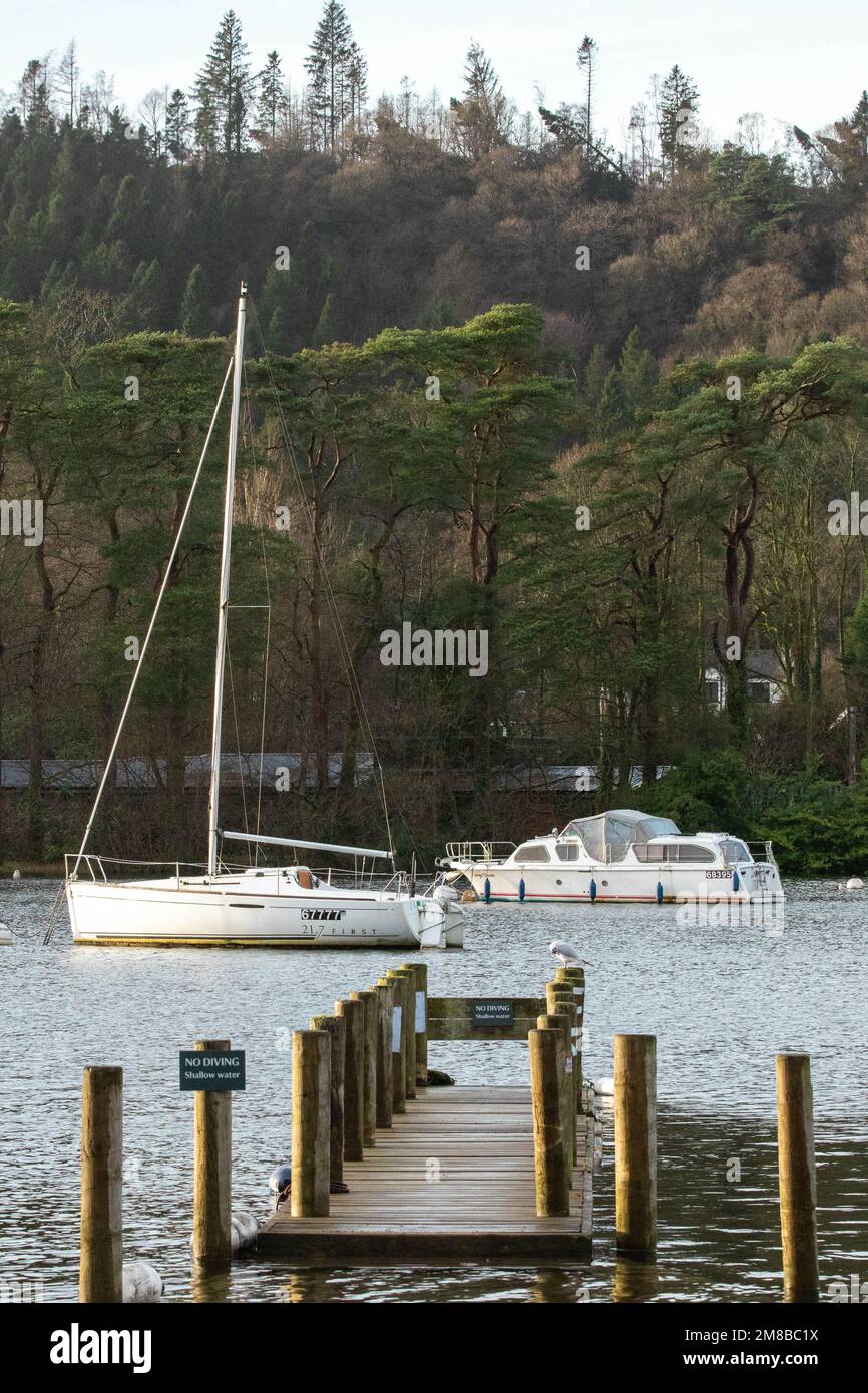 Jetée sur le lac Windemere menant à quelques bateaux lors d'une journée nuageux au bord des montagnes Banque D'Images