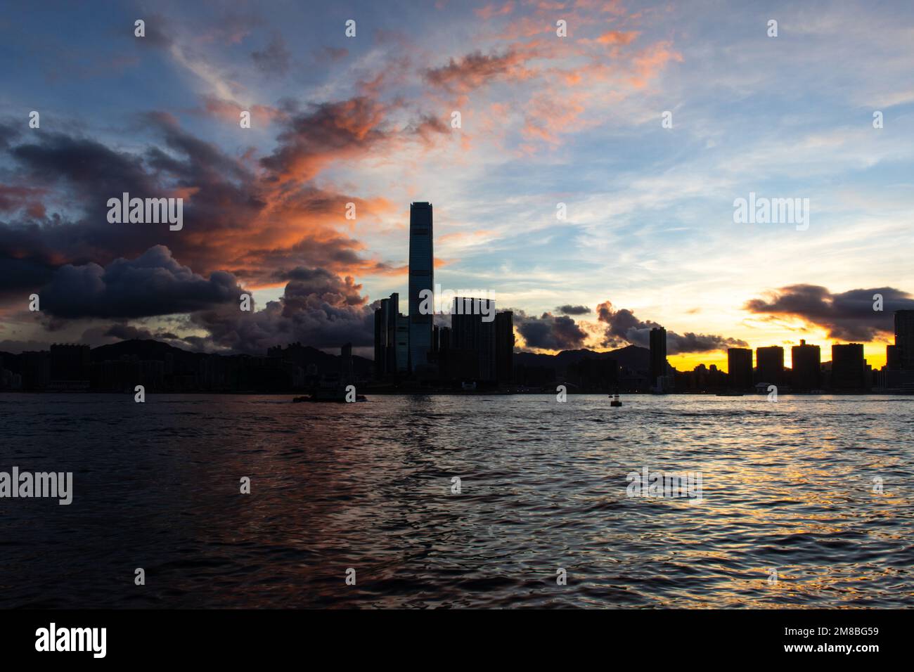 Le soleil se lève au-dessus de Kowloon, à Hong Kong. Mer au premier plan. Bâtiments en silhouette. Banque D'Images
