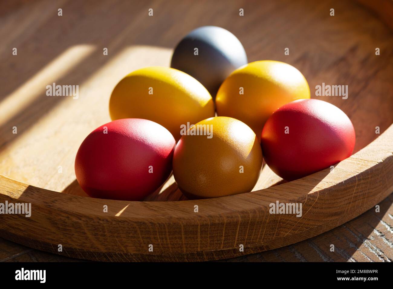 Six œufs de Pâques aux couleurs vives se trouvent sur un plateau en bois au soleil Banque D'Images
