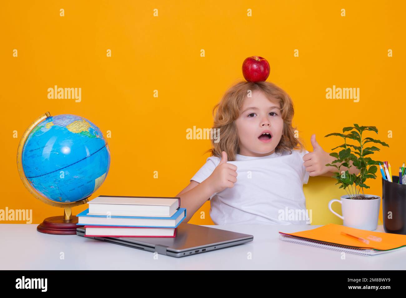 Enfant garçon de l'école primaire avec livre sur fond jaune isolé. Petit étudiant, pupille intelligente de nerd prêt à étudier. Concept d'éducation et Banque D'Images