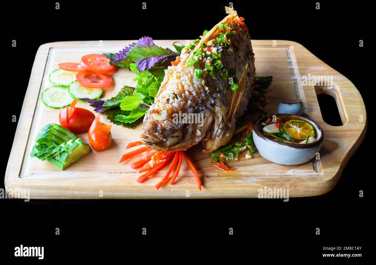 Perchaude grillée en pâte avec légumes et légumes verts sur un tableau de hachage en bois isolé sur fond noir vue latérale Banque D'Images