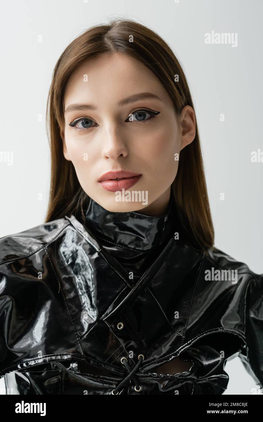 Portrait d'une femme élégante avec des vêtements de maquillage et de latex regardant l'appareil photo isolé sur gris, image de stock Banque D'Images