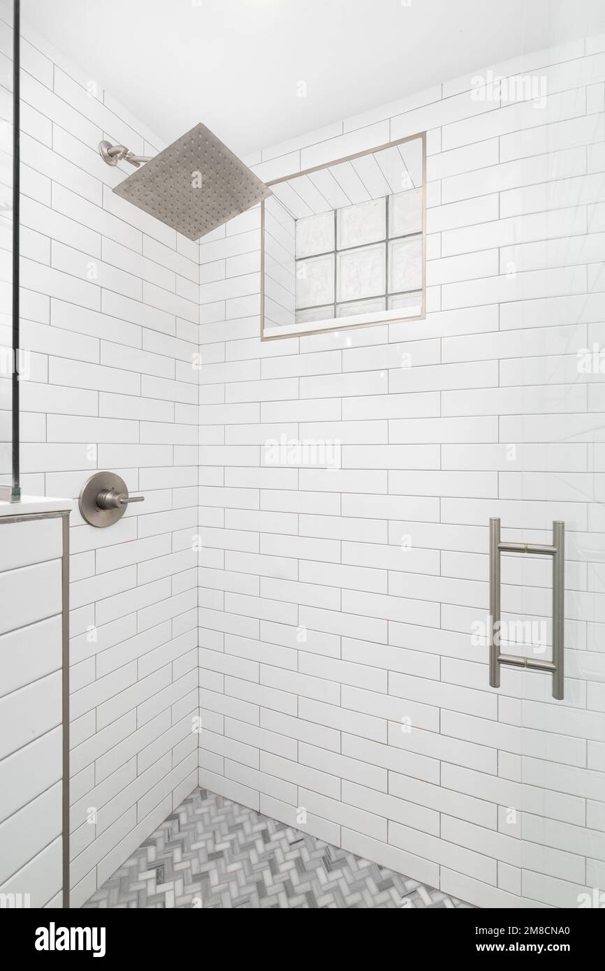 Une douche à l'italienne avec des murs de carreaux de métro blancs, un sol carrelé en marbre à chevrons et une fenêtre en blocs de verre. Banque D'Images