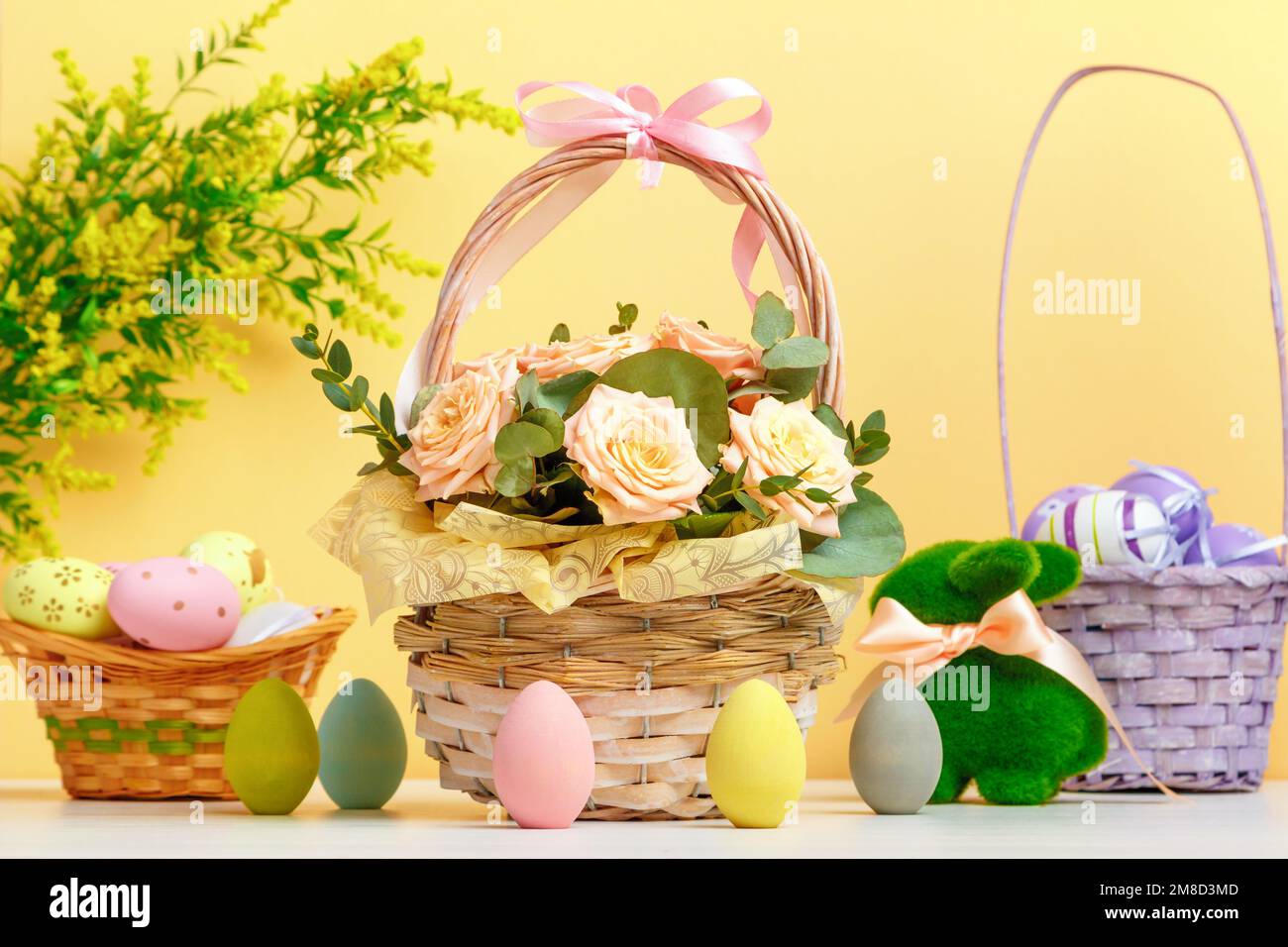 La composition de Pâques reste la vie. Un panier avec des fleurs et des œufs, un lapin jouet sur la table. Banque D'Images