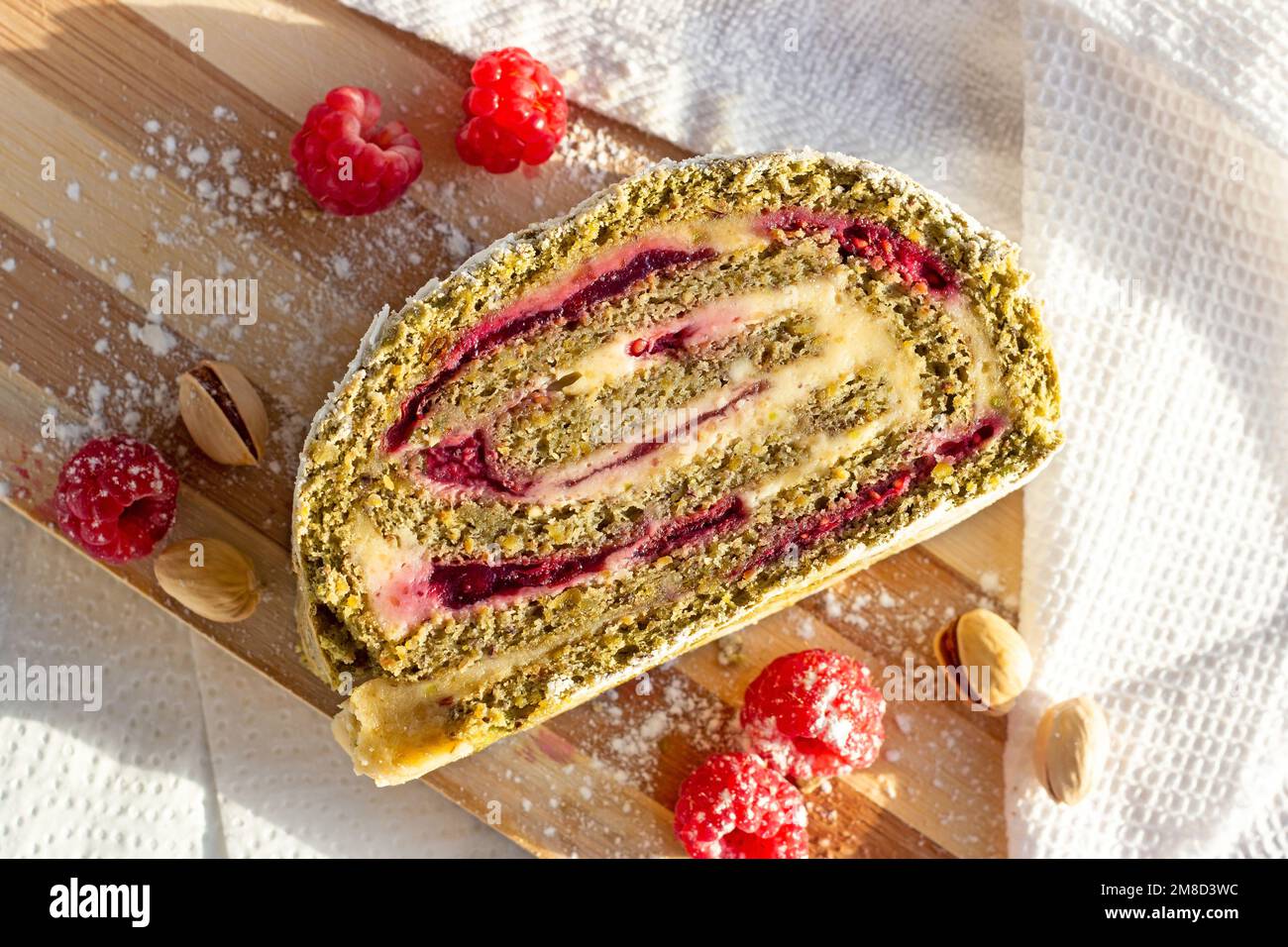 Tranche de roulade de pistache verte meringue avec confiture de framboise sur fond de bois clair dans la vue du dessus de la cuisine. Banque D'Images