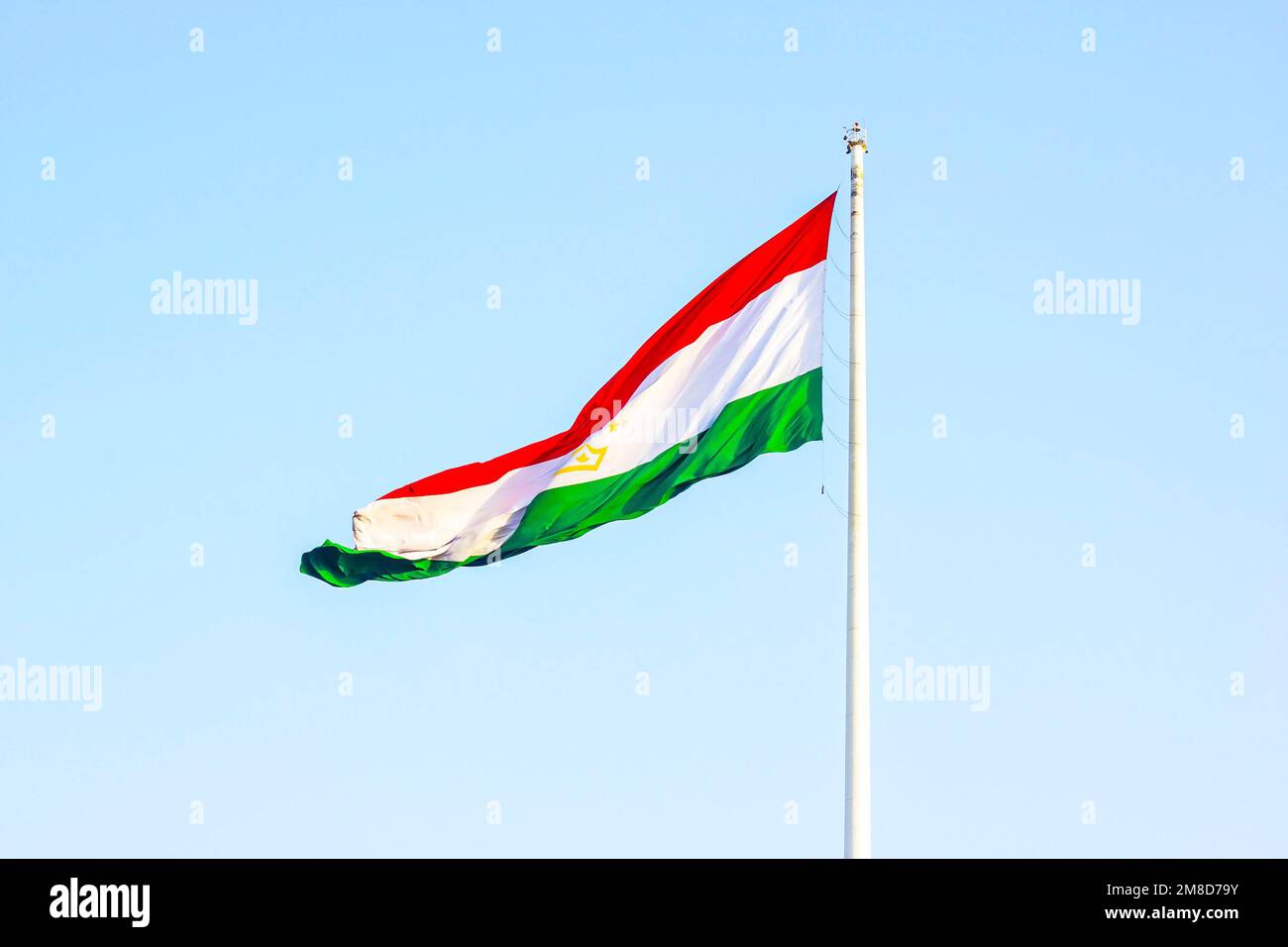 Drapeau national rouge, blanc et vert du Tadjikistan sur le mât contre le ciel bleu. Banque D'Images