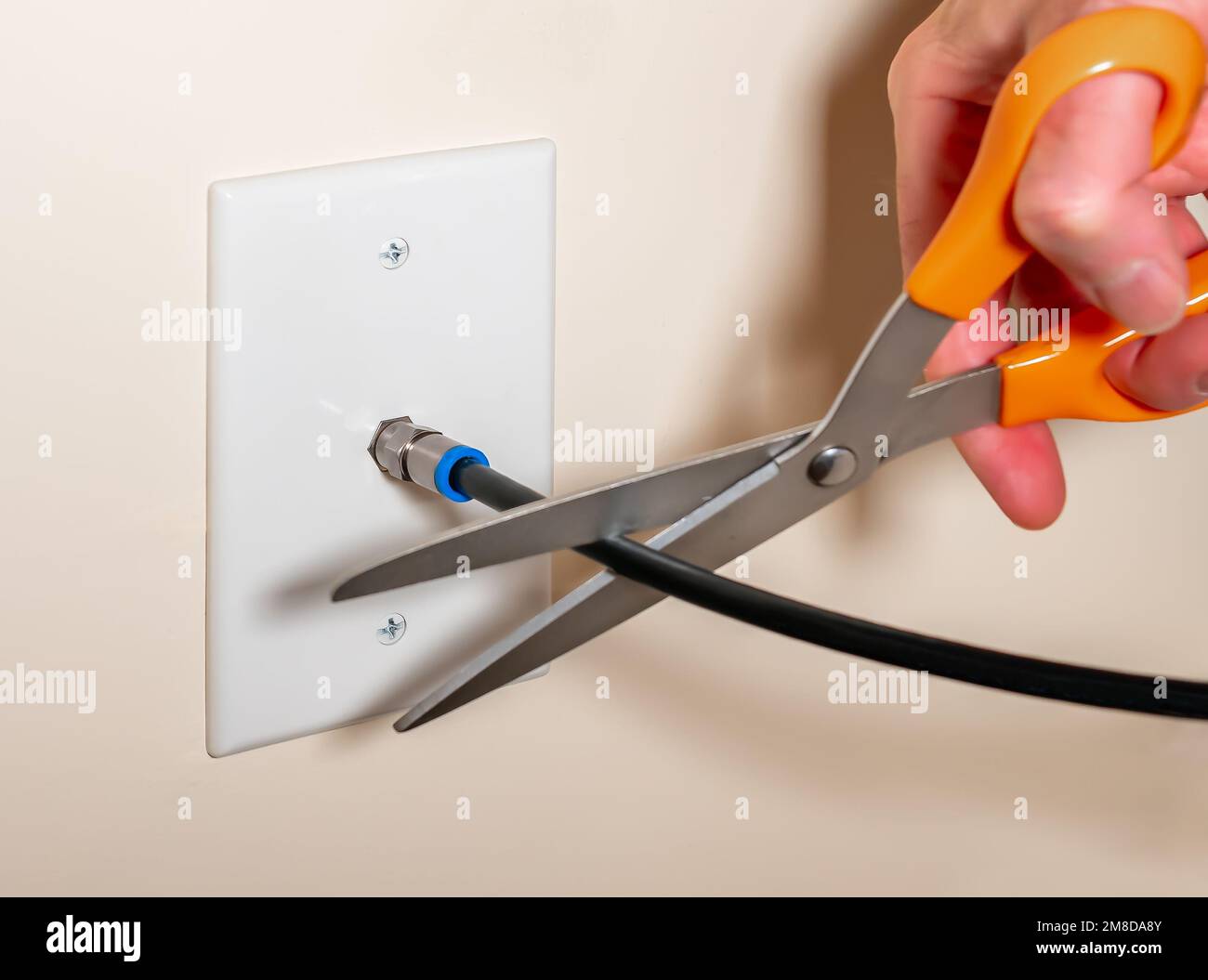 Annulation du service de télévision par câble en coupant la connexion du câble coaxial. Gros plan de la main masculine en utilisant des ciseaux pour déconnecter l'abonnement à la télévision. Banque D'Images