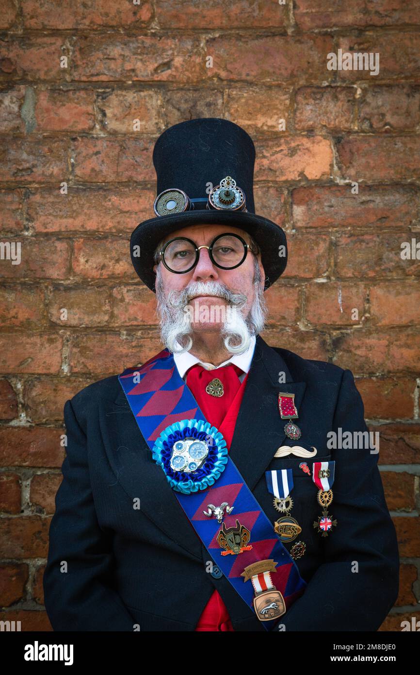 Portrait d'un ancien homme distingué steampunk portant un chapeau avec des lunettes attachées et un costume de cérémonie . Il a une magnifique barbe mauviée. Banque D'Images