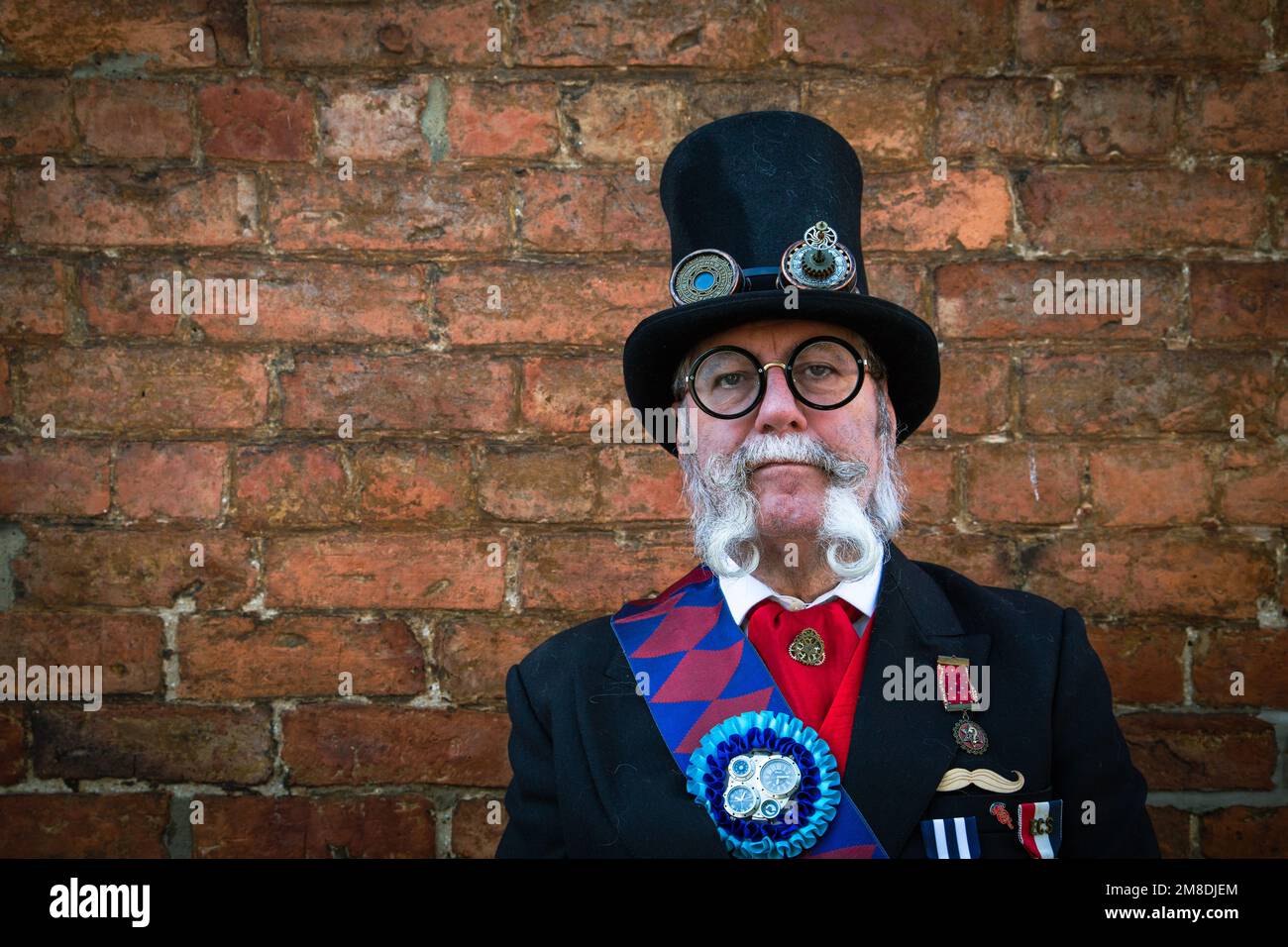 Portrait d'un ancien homme distingué steampunk portant un chapeau avec des lunettes attachées et un costume de cérémonie . Il a une magnifique barbe mauviée. Banque D'Images