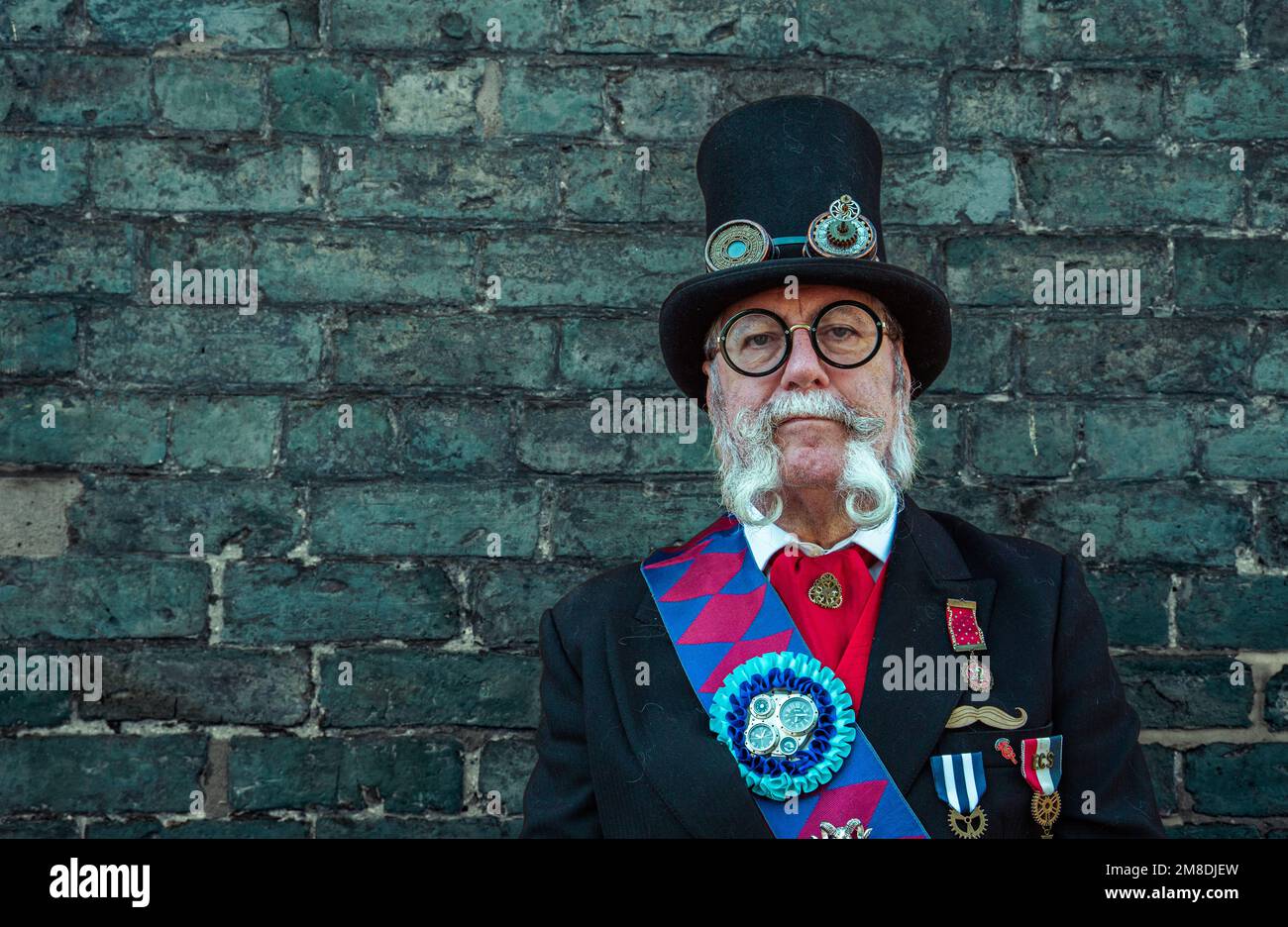 Portrait d'un ancien homme distingué steampunk portant un chapeau avec des lunettes attachées et un costume de cérémonie . Il a une magnifique barbe mauviée. Banque D'Images