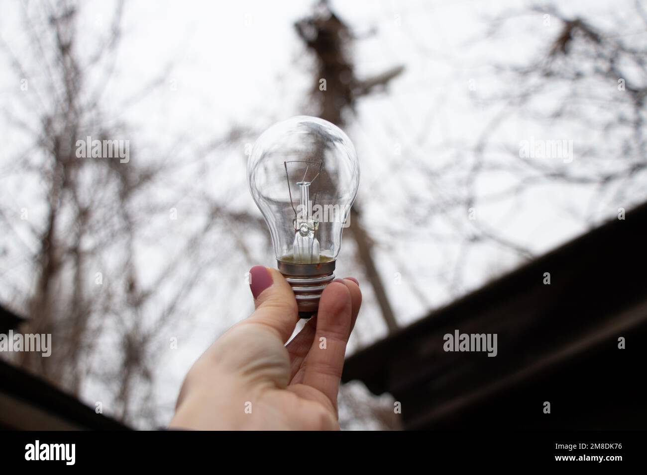 Une ampoule à incandescence dans les mains d'une fille contre le ciel, un vozli à la maison, des gens sans lumière, lumière Banque D'Images