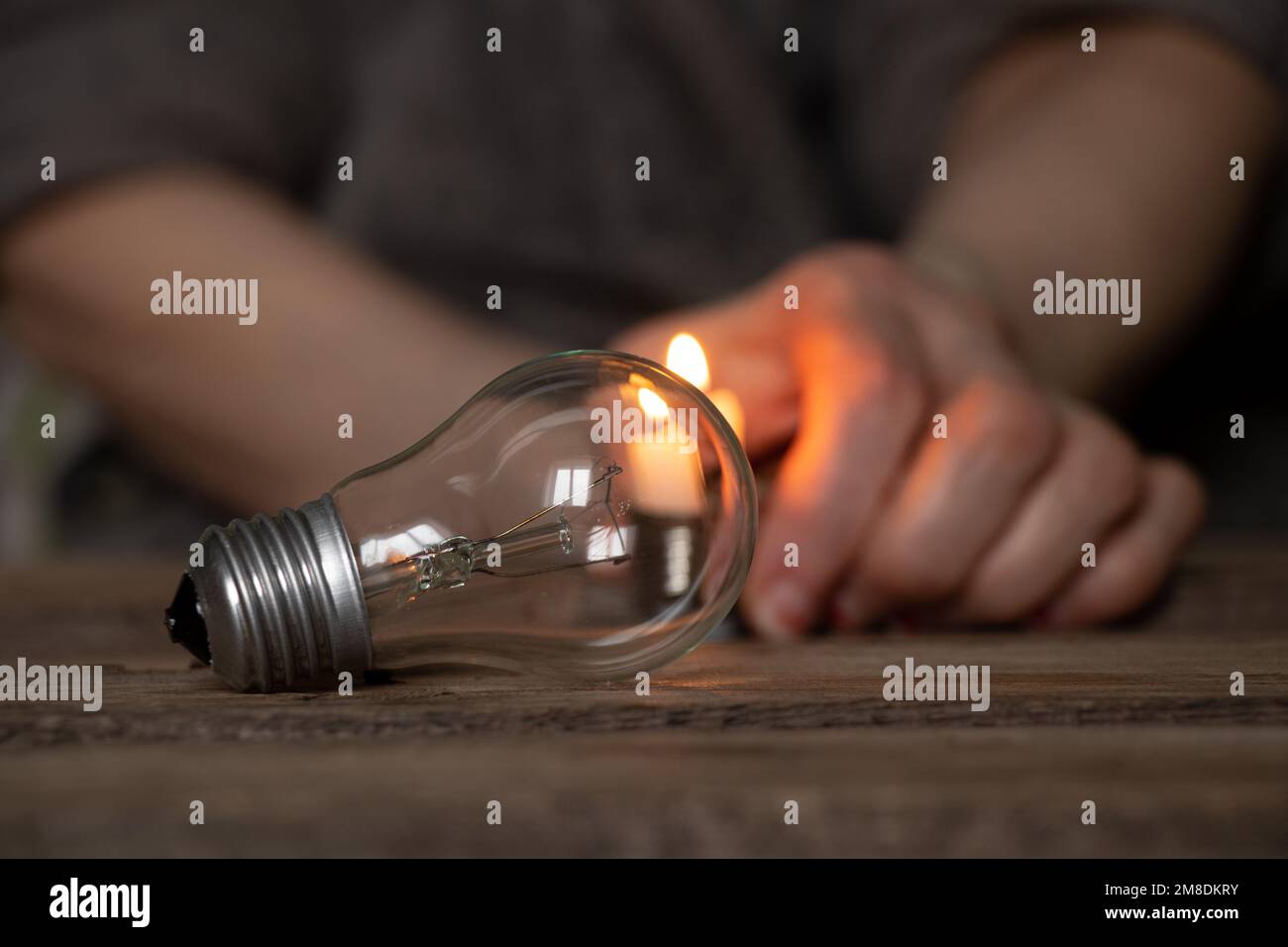 Une ampoule à incandescence et une bougie dans les mains d'une vieille femme sur une table en bois, des gens sans lumière, la lumière d'une bougie quand il n'y a pas de l Banque D'Images