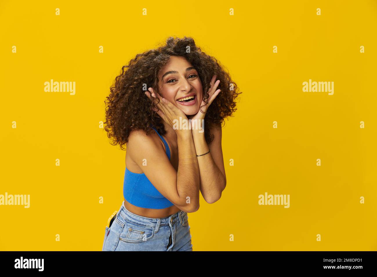 Femme aux cheveux bouclés afro dans un t-shirt bleu. signes de fond jaune avec ses mains, regarder dans la caméra, sourire avec les dents et le bonheur, copier Banque D'Images